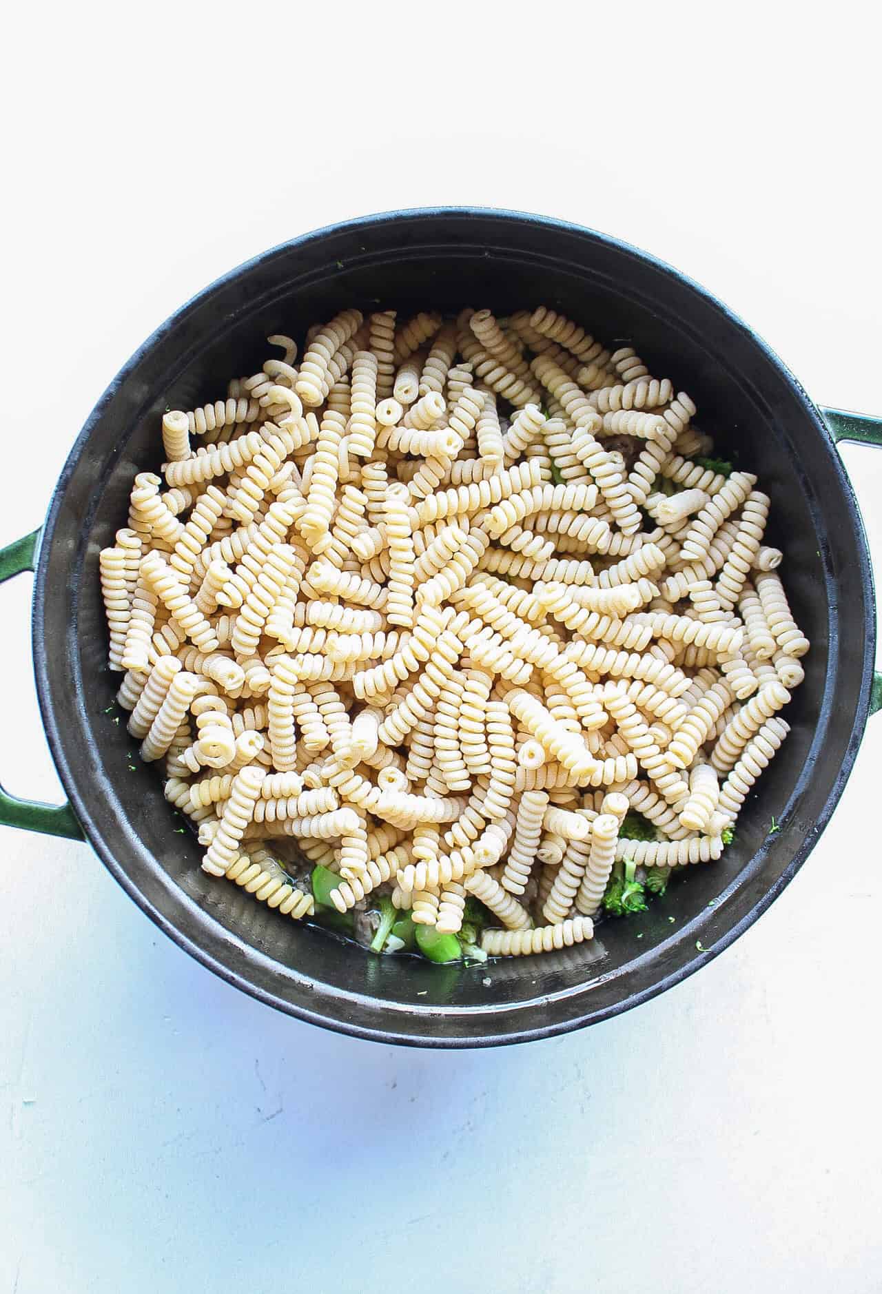 Dry pasta added to a dutch oven with broccoli and browned ground pork sausage.