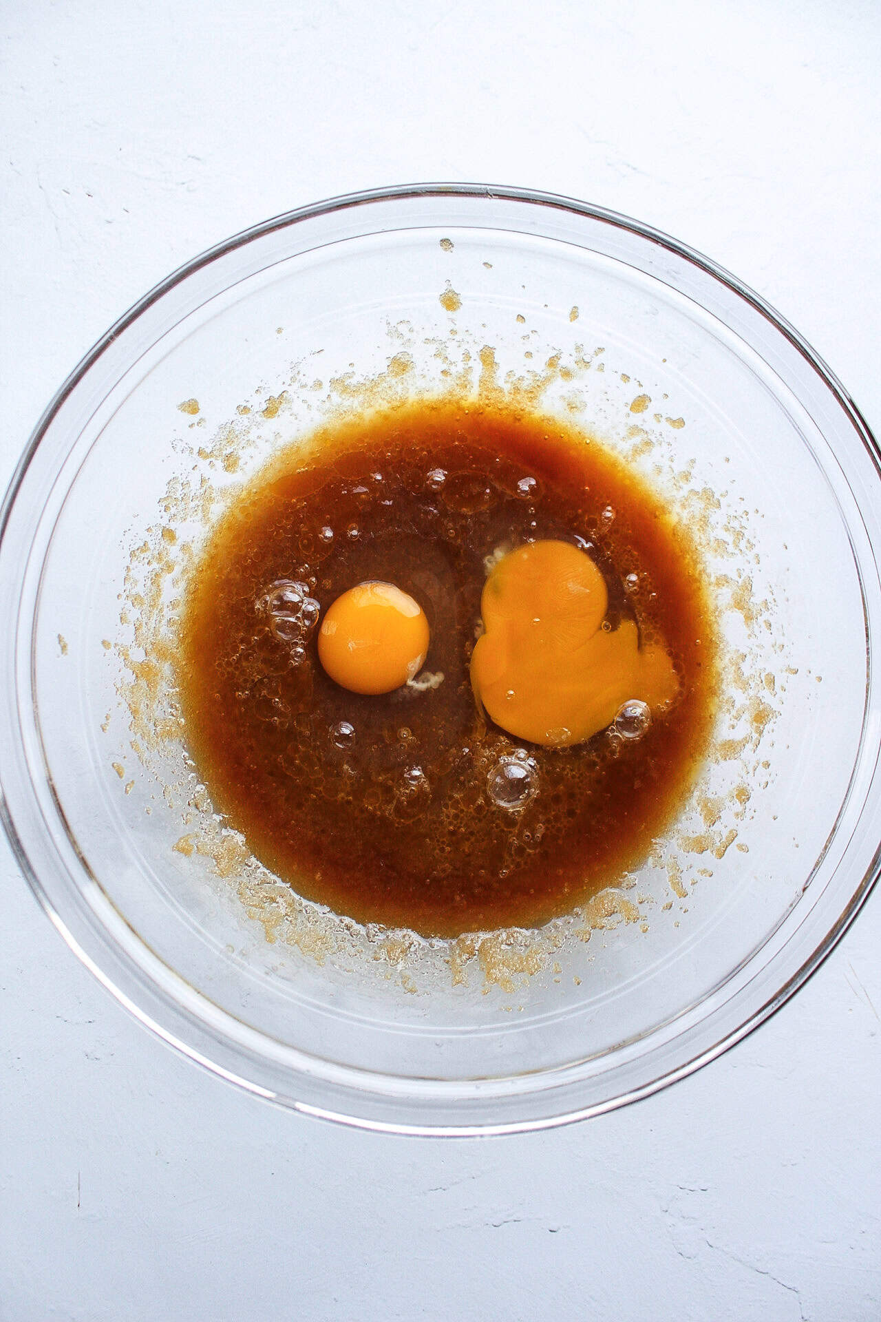 Eggs added to a bowl of whisked melted butter and sugar.