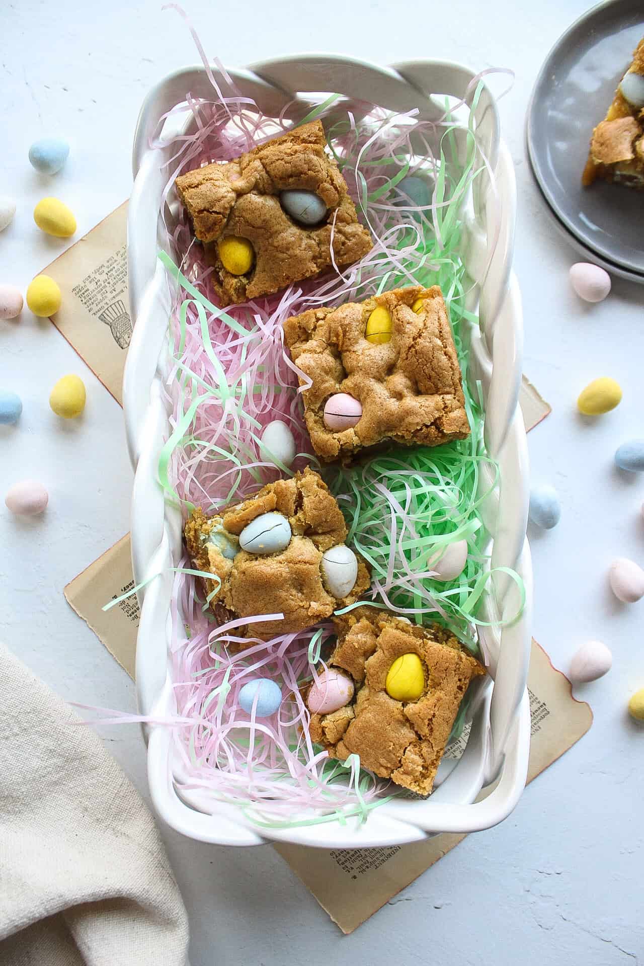 Four easter egg blondies in a basket with green and pink fake grass.