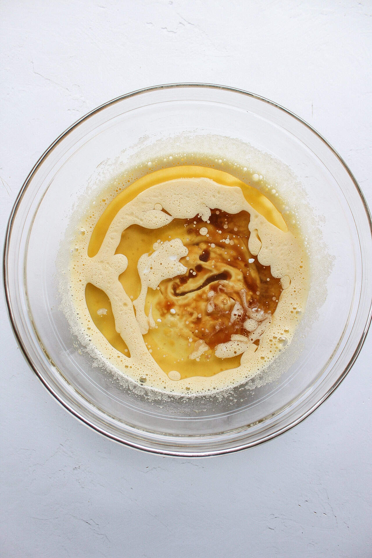 Wet ingredients such as eggs, sugar, vanilla extract, greek yogurt, and oil mixed together in a bowl.