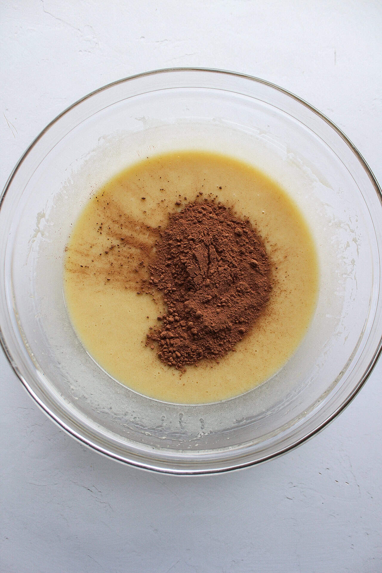 Cocoa powder added to a bowl of wet muffin ingredients.