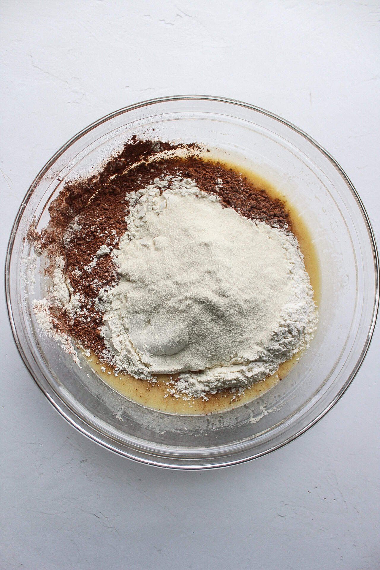 Dry ingredients like baking powder, baking soda, baking salt, flour, and protein powder added to a bowl of wet muffin ingredients.