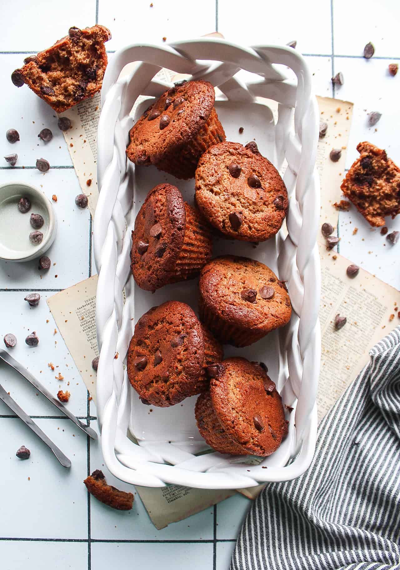 Six chocolate protein muffins in a porcelain basket with chocolate chips surrounding.