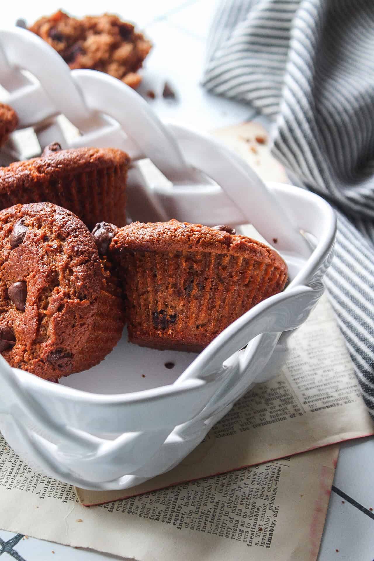 Close up of Six chocolate protein muffins in a porcelain basket with chocolate chips surrounding.