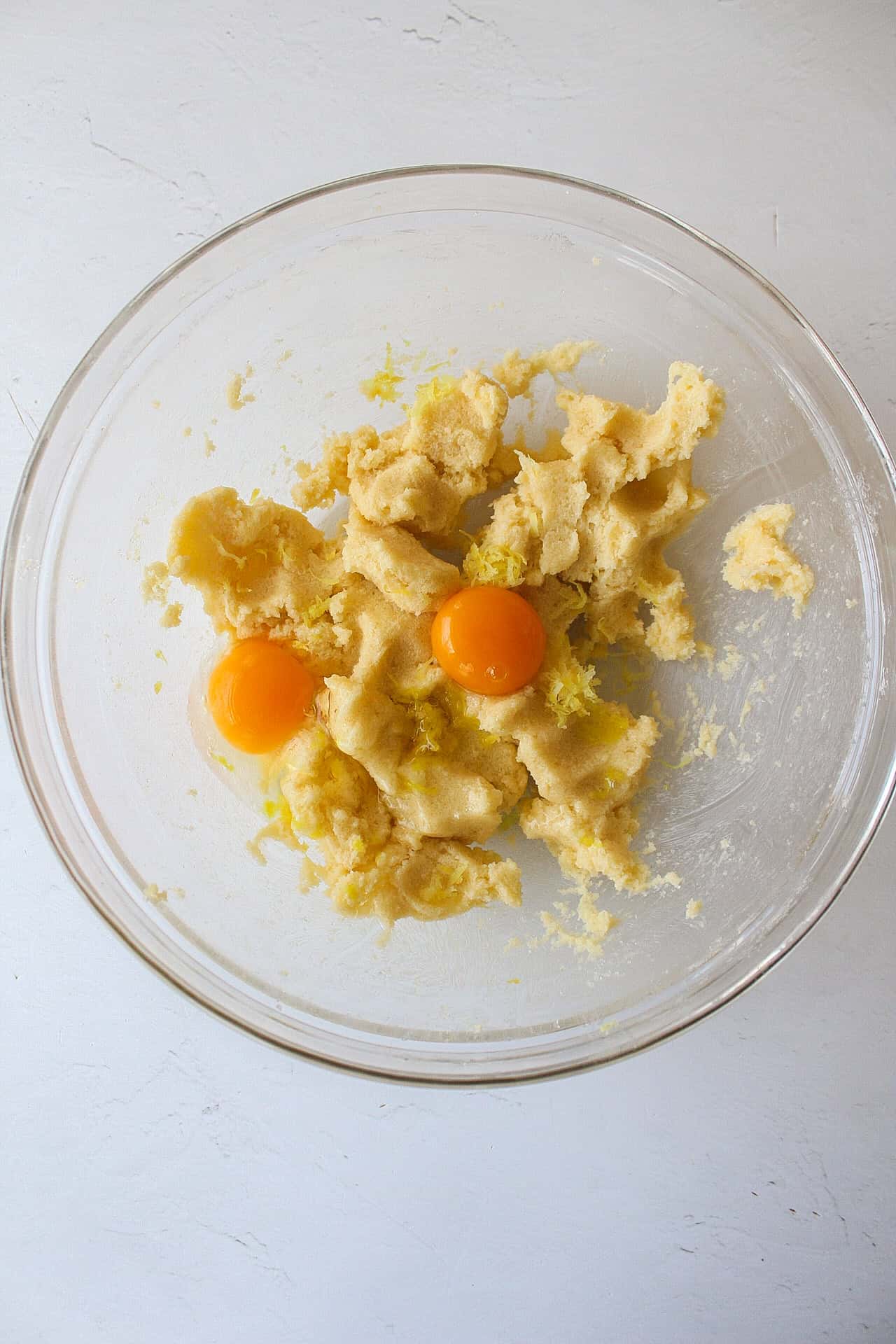 One egg, one egg yolk added to a bowl with with creamed butter and sugar.