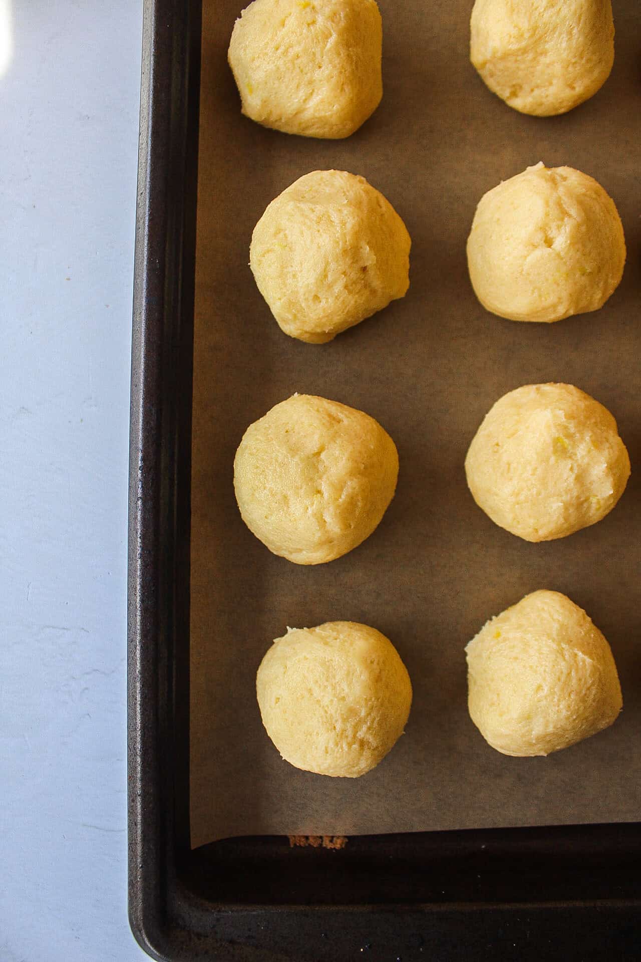 Six lemon sugar cookie dough balls on a baking sheet.