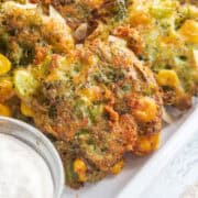 Close up of broccoli cheddar fritters with a dipping sauce in a small dish.