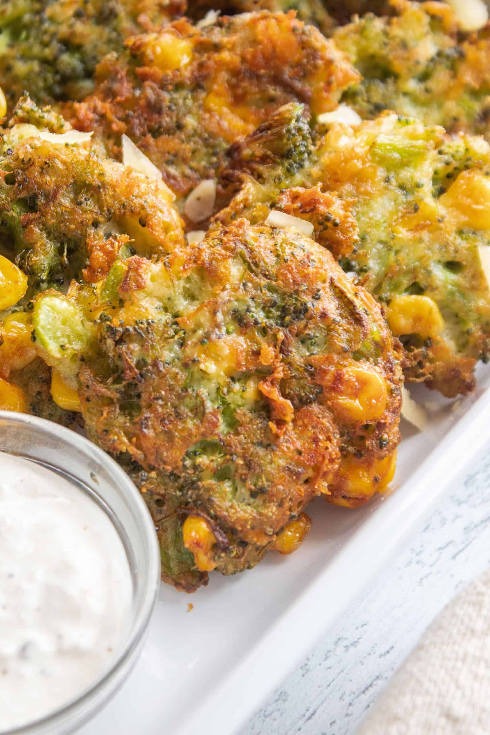 Close up of broccoli cheddar fritters with a dipping sauce in a small dish.