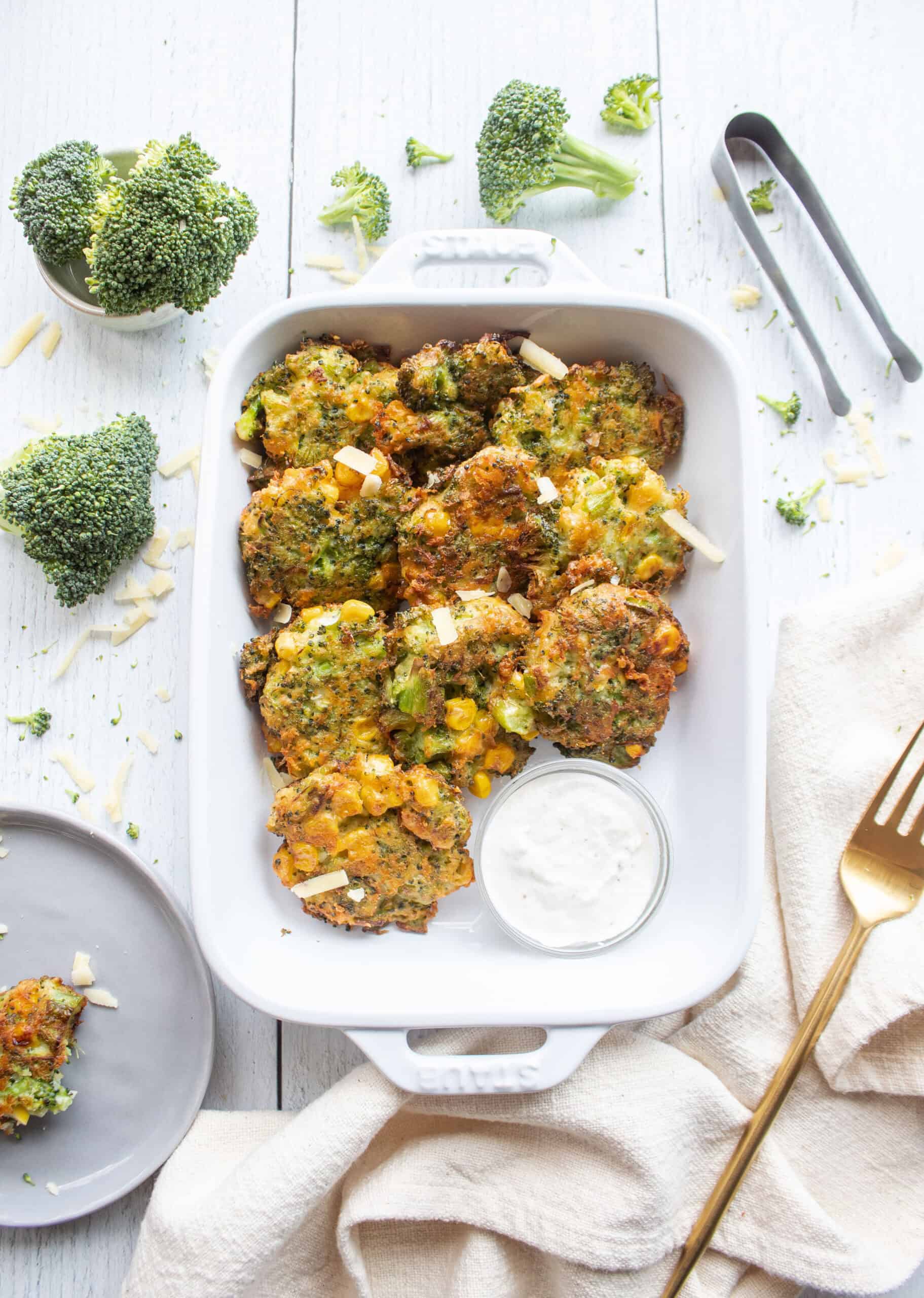 Broccoli cheddar fritters in a baking dish with a dipping sauce.