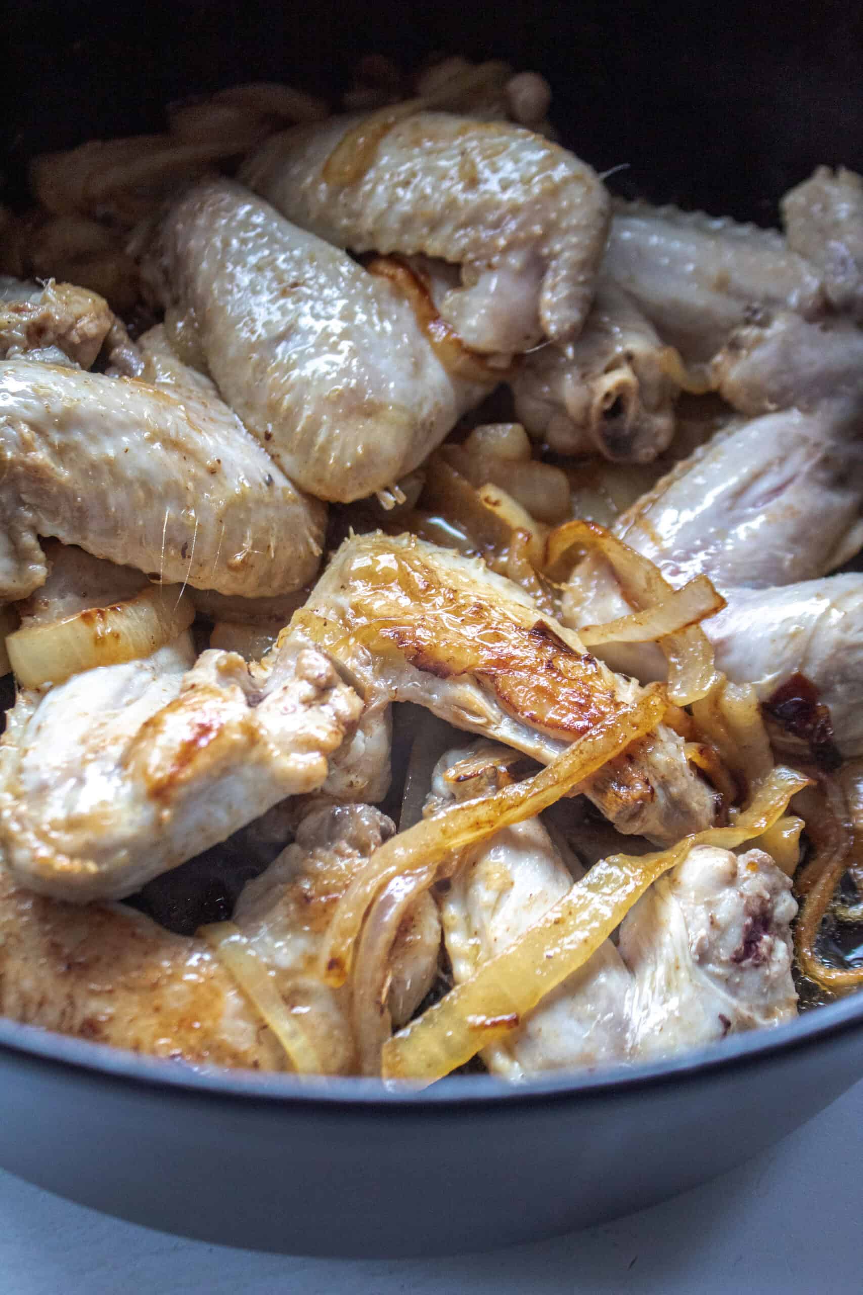 Browned chicken wings with onions in a dutch oven.