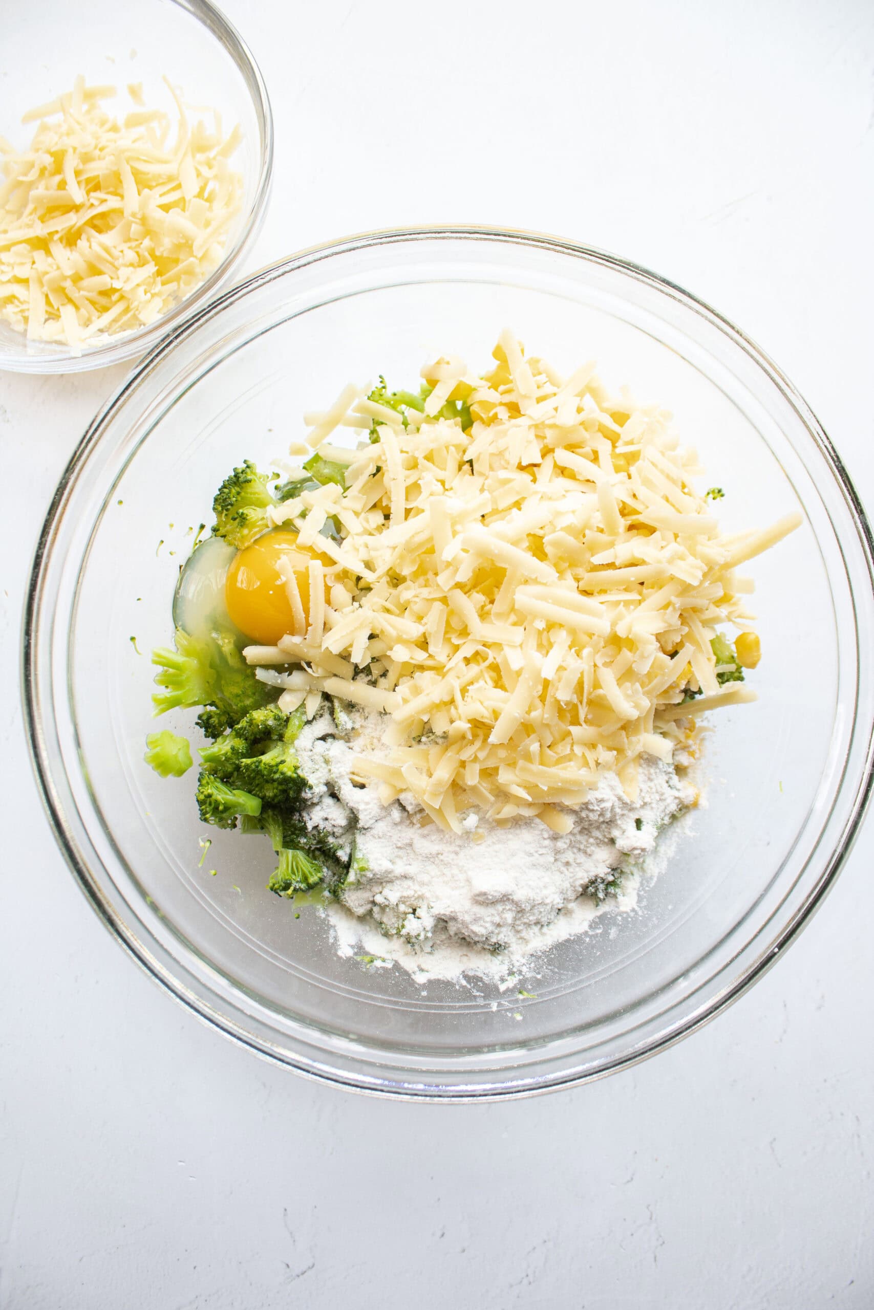 cheese added to a bowl of chopped broccoli, corn, egg, and flour.