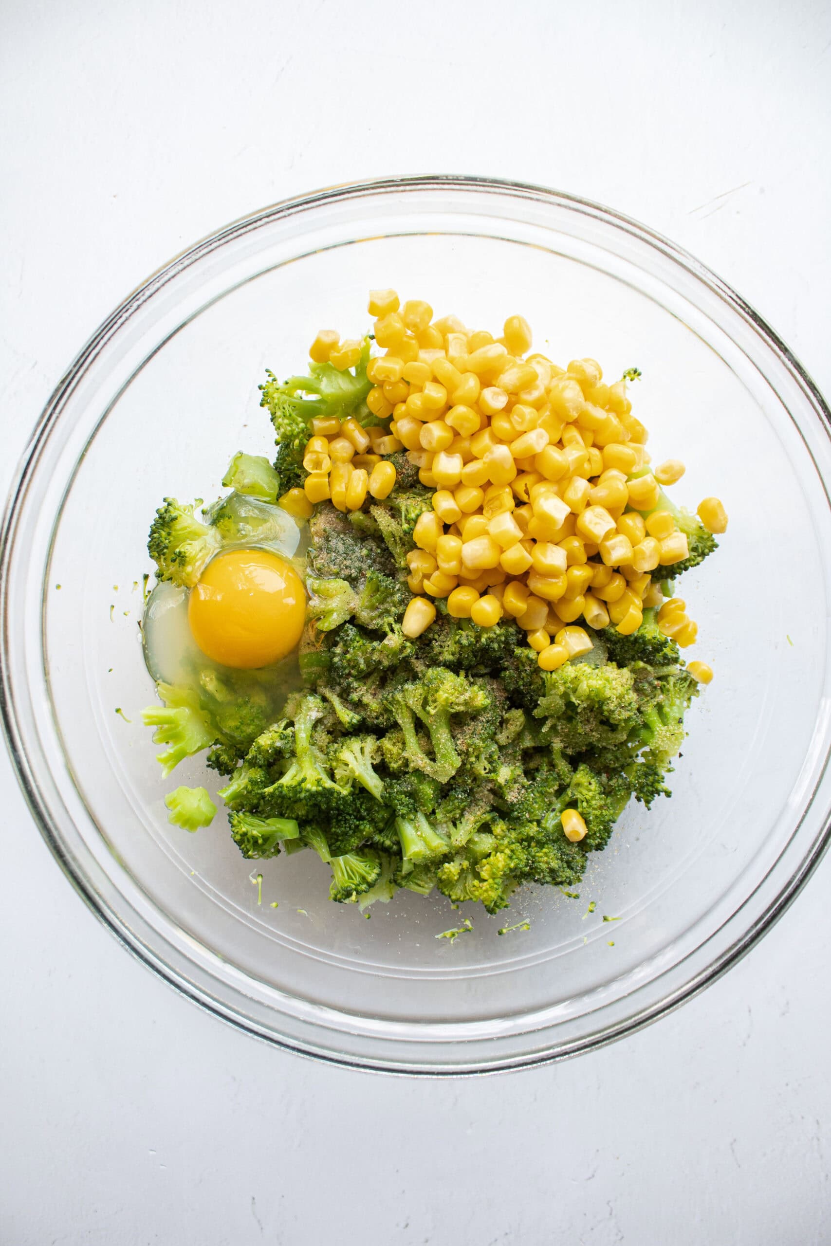 steamed and chopped broccoli in a bowl with corn, egg, and seasonings.