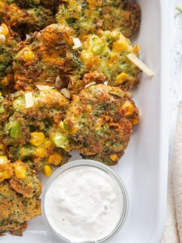 Close up of broccoli cheddar fritters with a dipping sauce in a small dish.