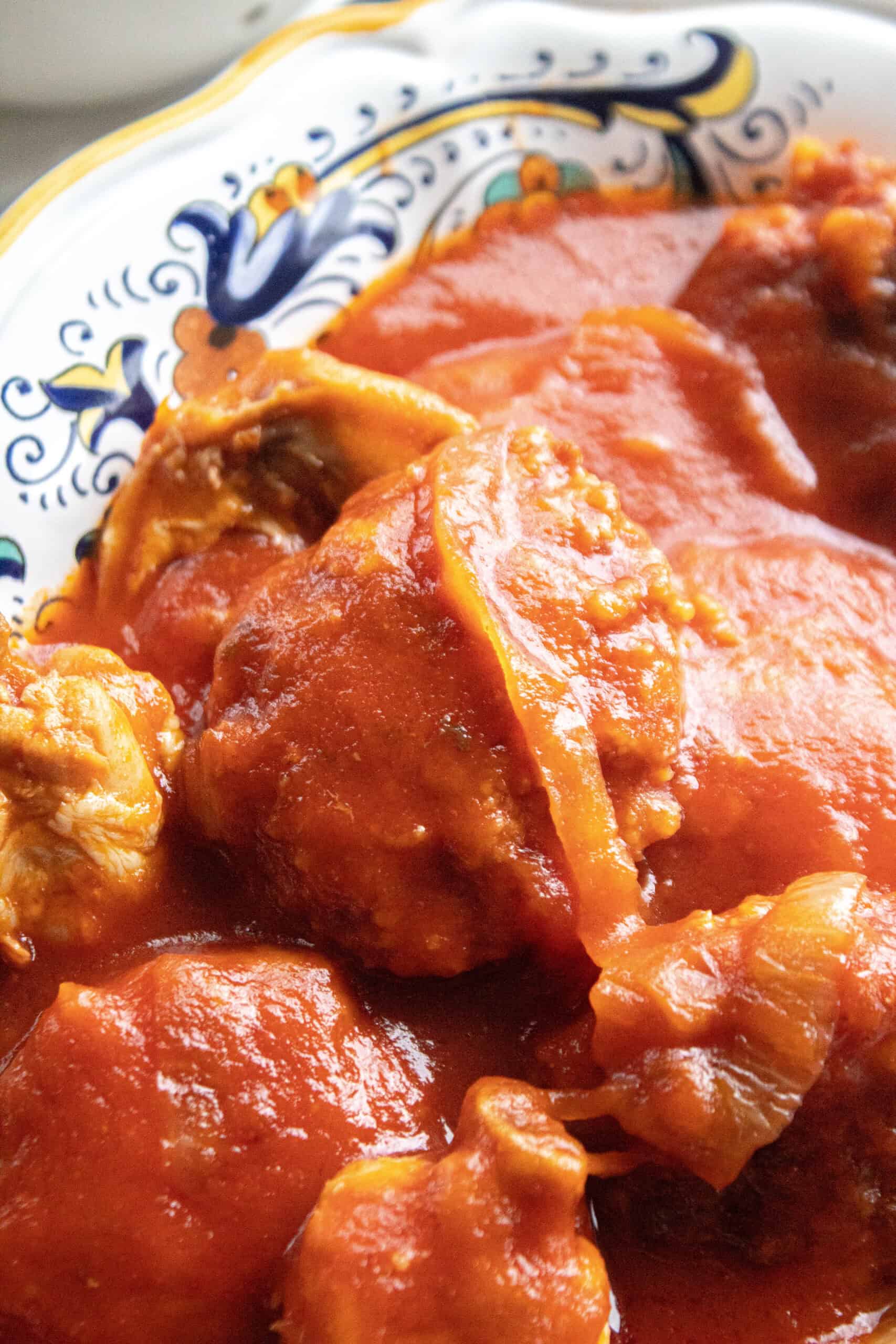 close up of a chicken patty with onions in red sauce.