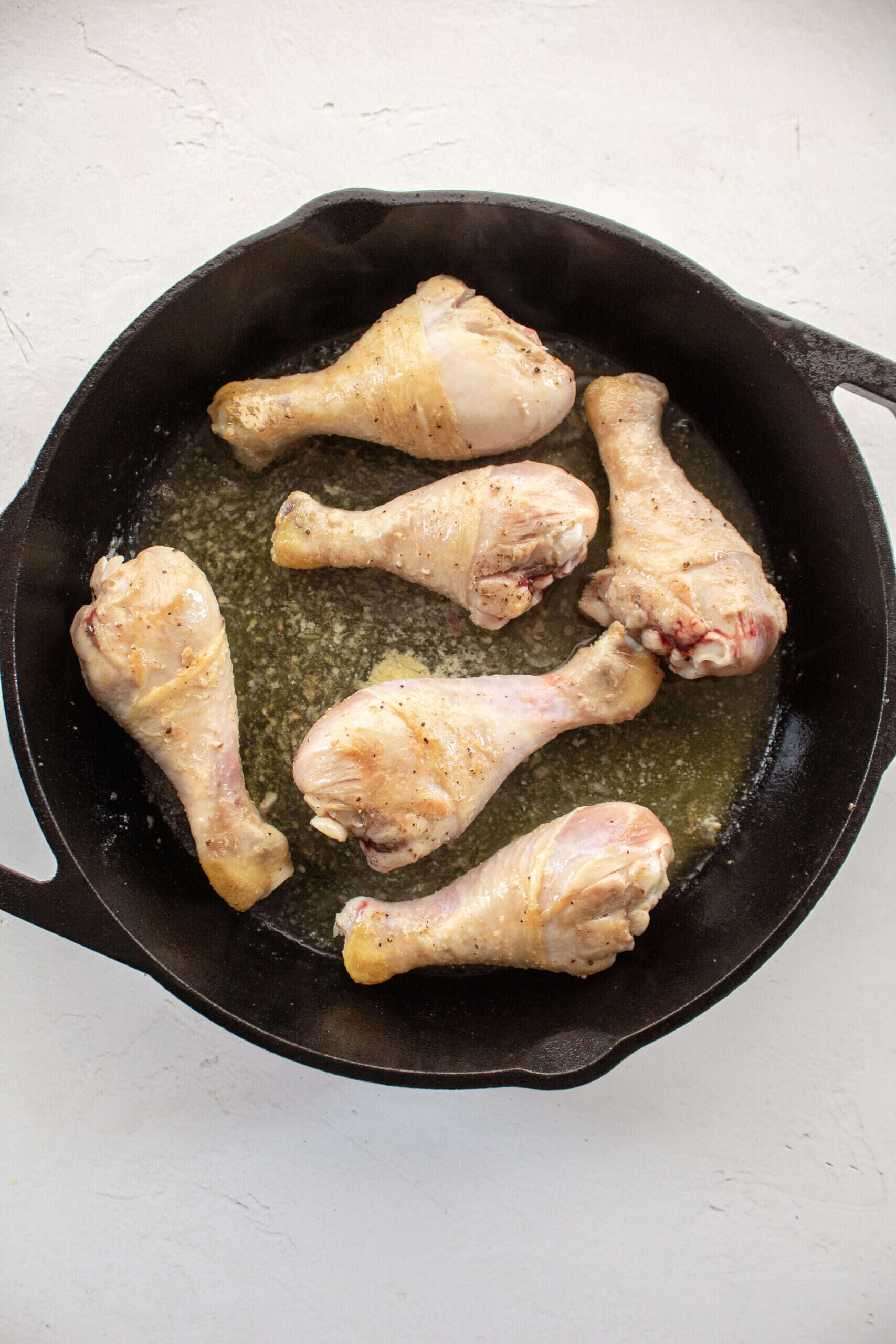 seared chicken drumsticks in a cast iron skillet with butter.