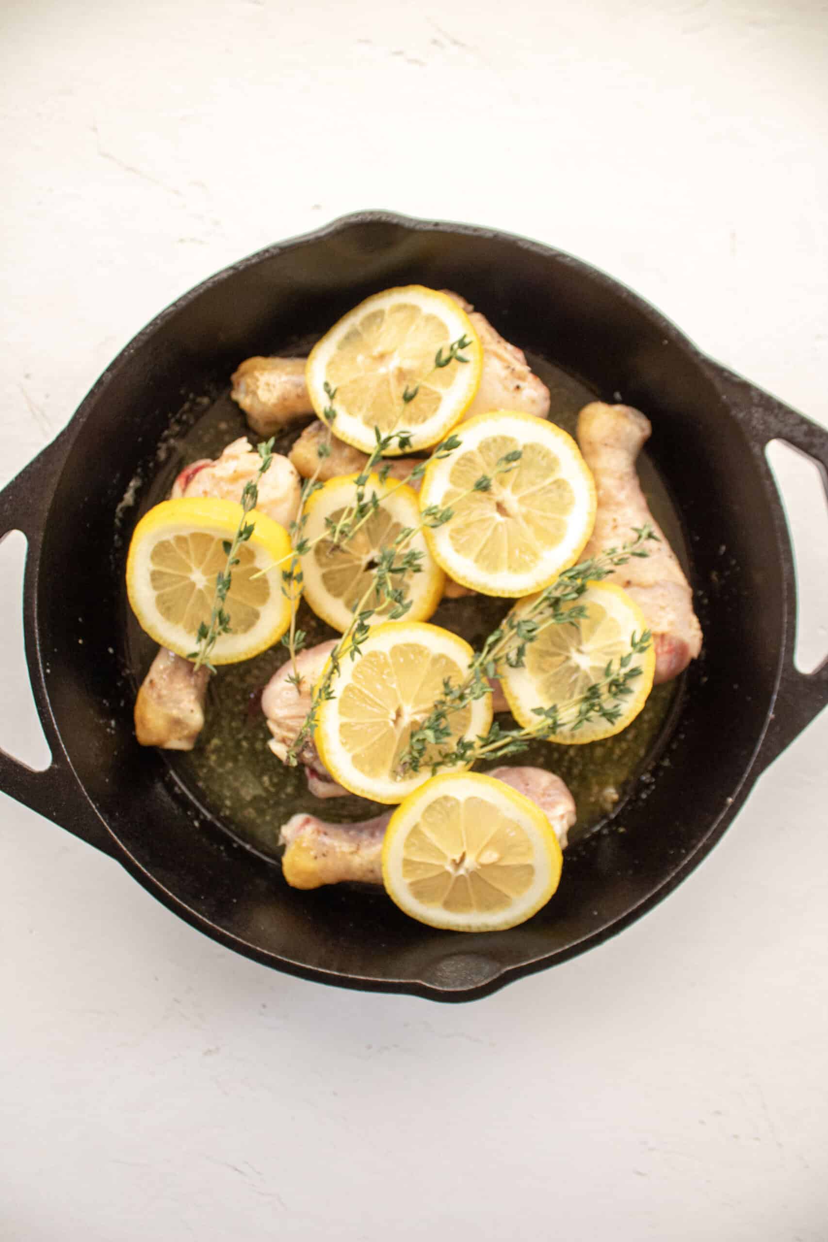 seared chicken drumsticks in a cast iron with lemon and thyme.
