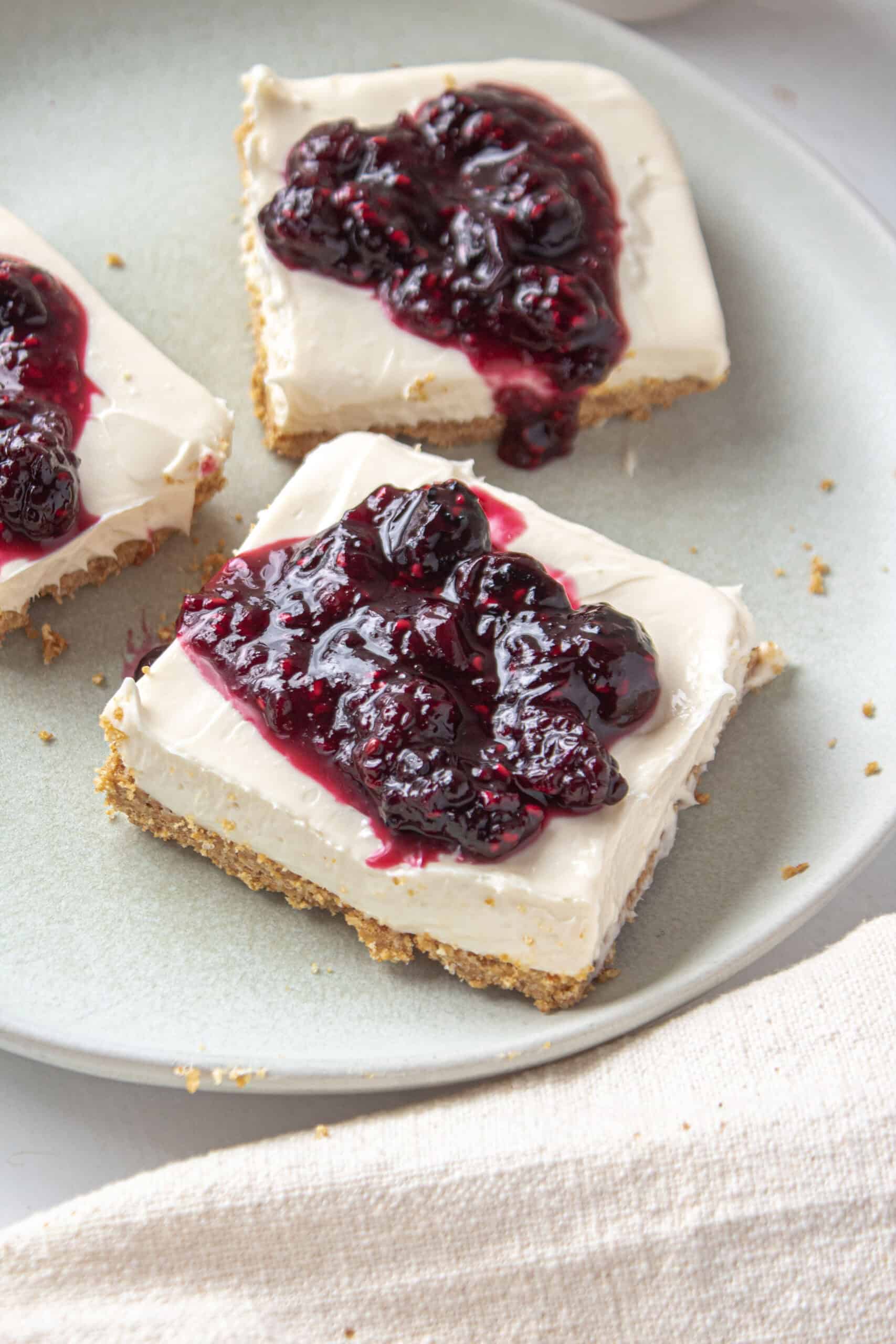 Close up of a cheesecake bar on a plate with berry compote on top.