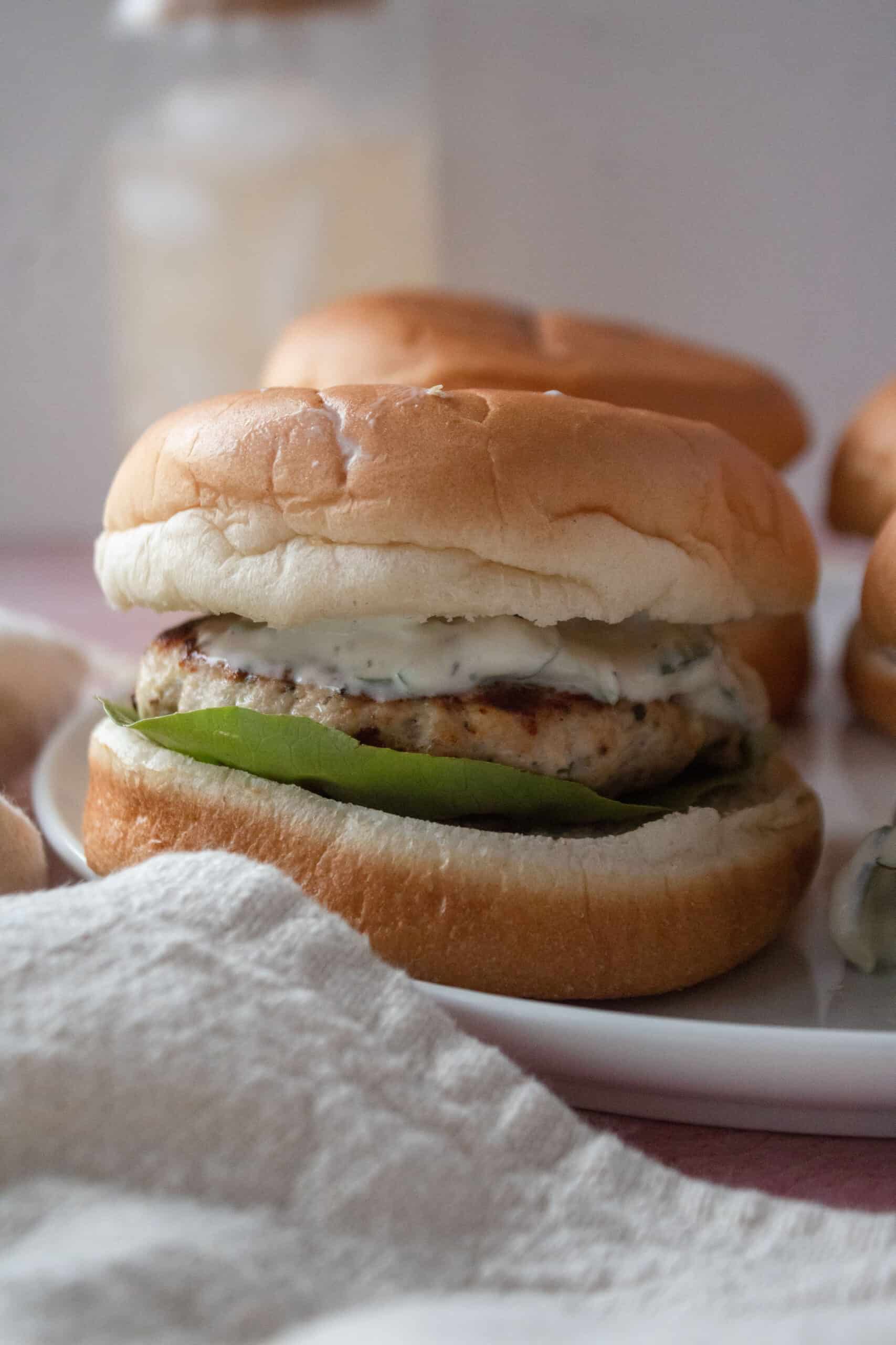 greek chicken burger on a plate with tzatziki sauce.