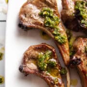 a few lamb chops on a plate with chimichurri sauce on top.
