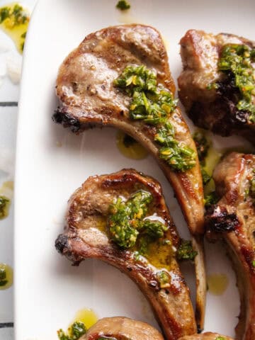 a few lamb chops on a plate with chimichurri sauce on top.