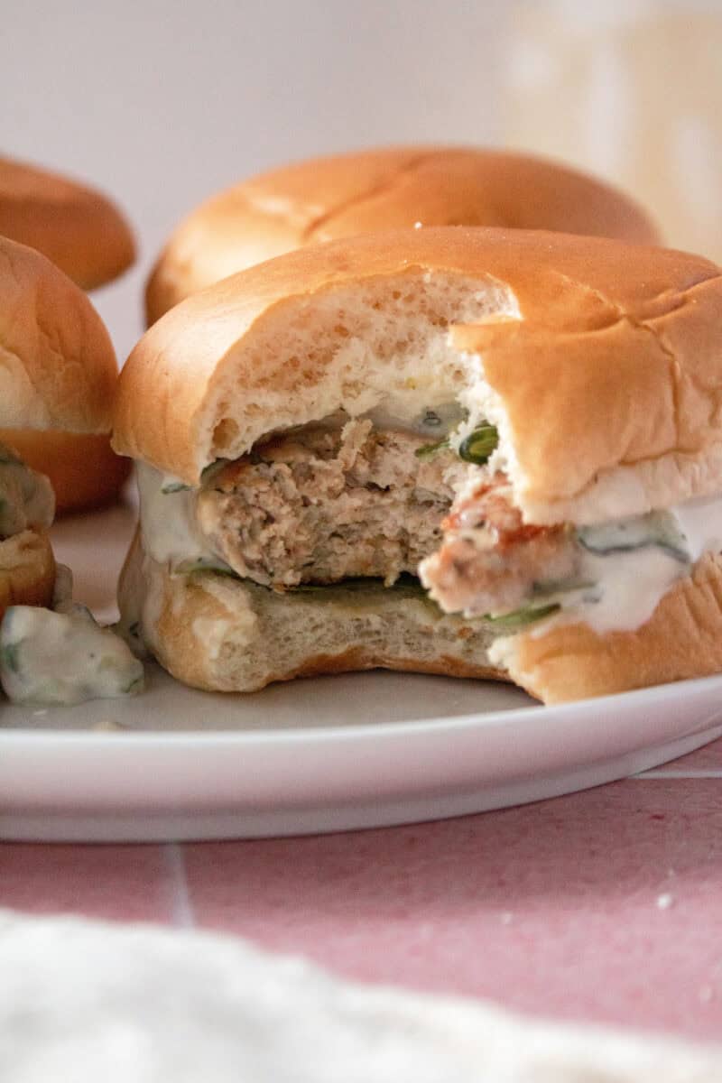 close up of a greek chicken burger on a plate with a bite missing.