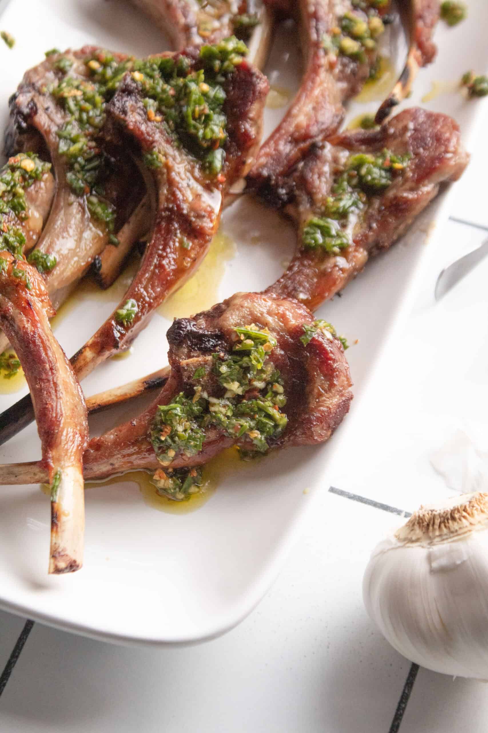 close up of lamb chops on a plate with chimichurri sauce on top.