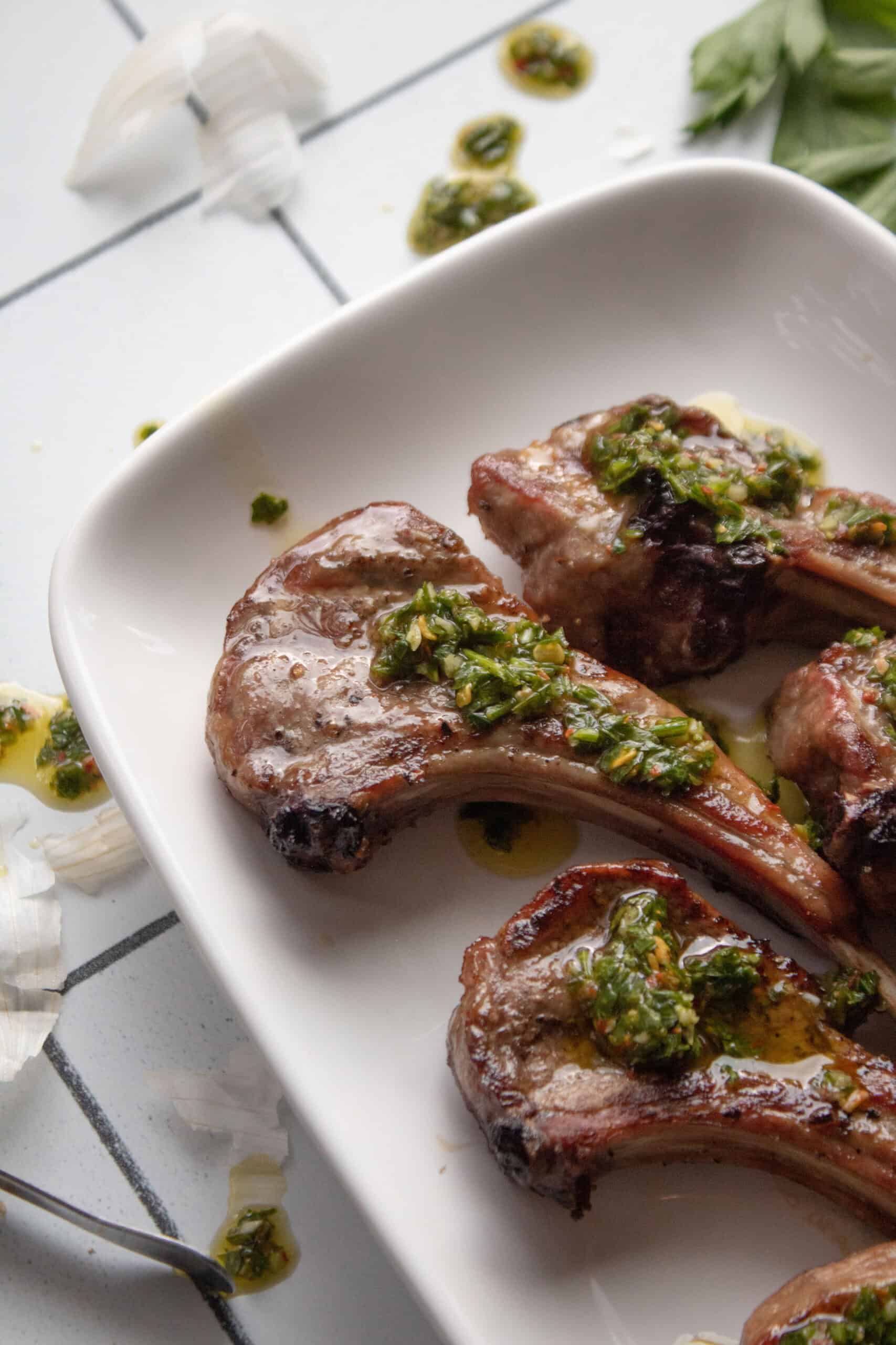 lamb chops on a plate with chimichurri sauce on top.