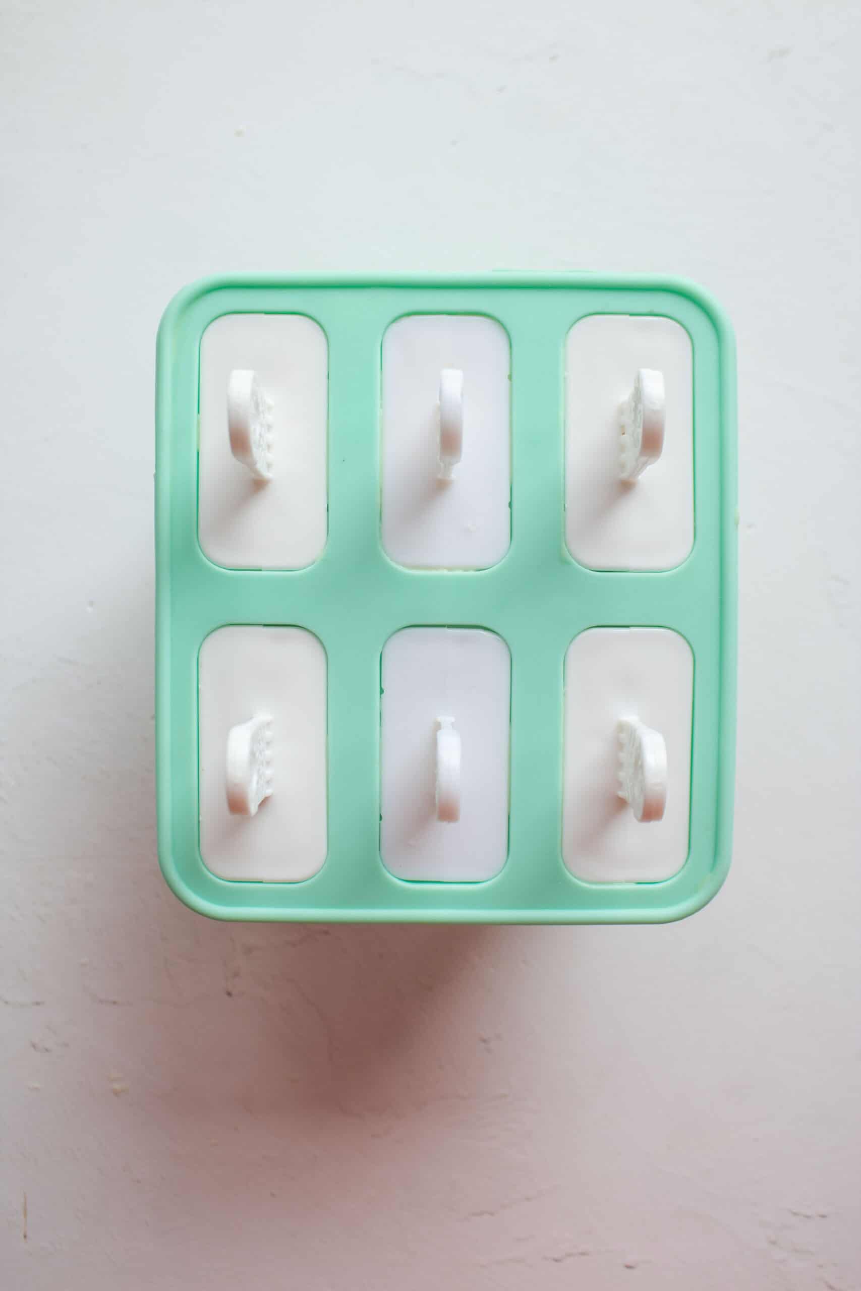a silicon popsicle mold with six popsicle sticks in them to make mango yogurt popsicles.