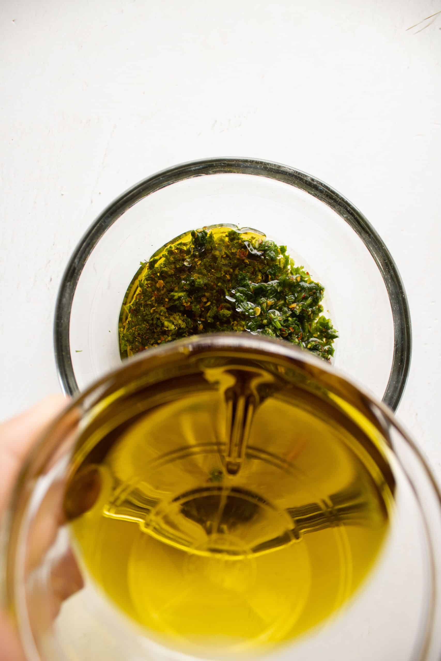 olive oil being added to fresh chopped ingredients of parsley, garlic, red pepper flakes, salt, and pepper.