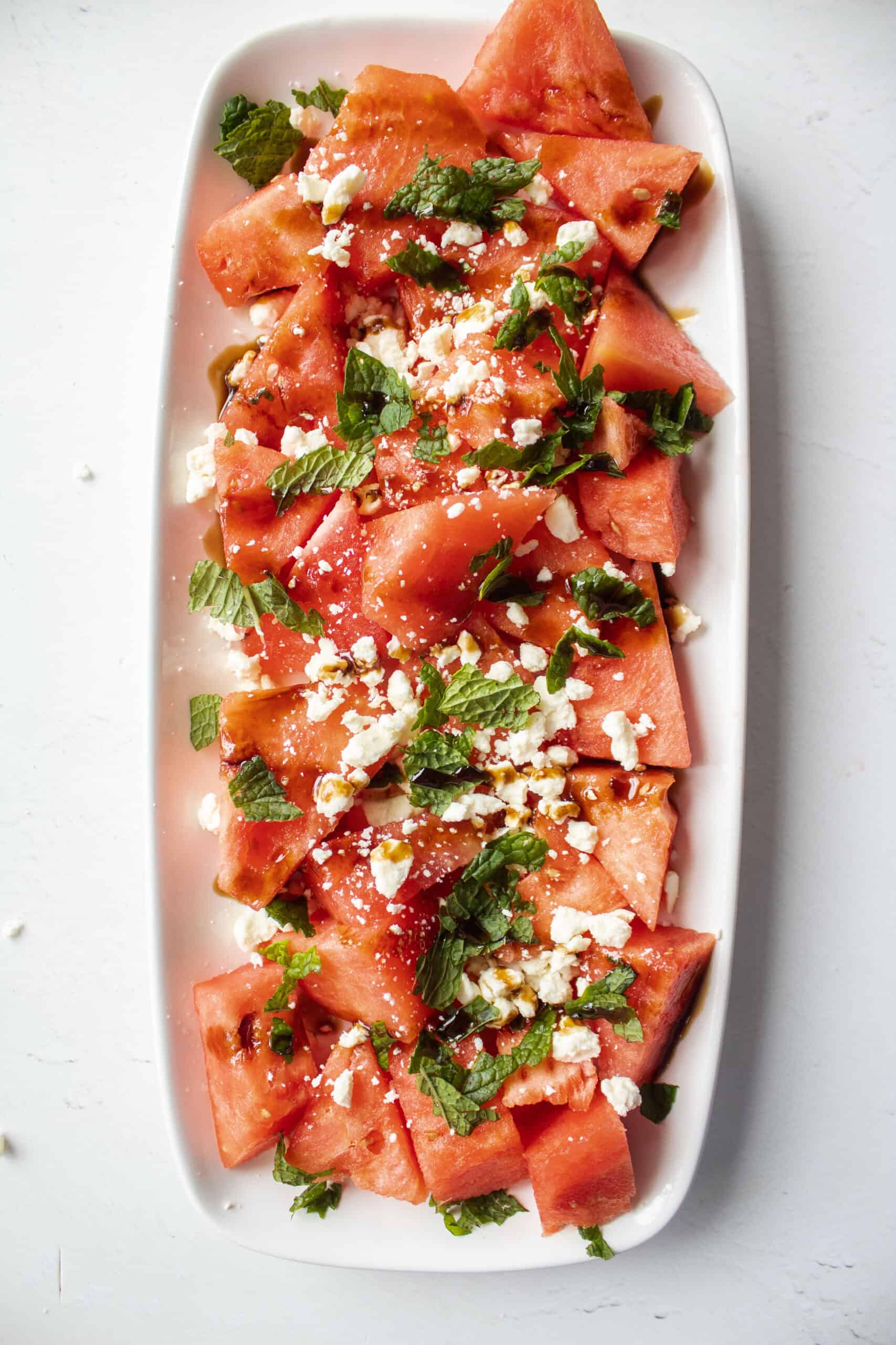Watermelon on a plate with crumbled feta, mint, and balsamic glaze.
