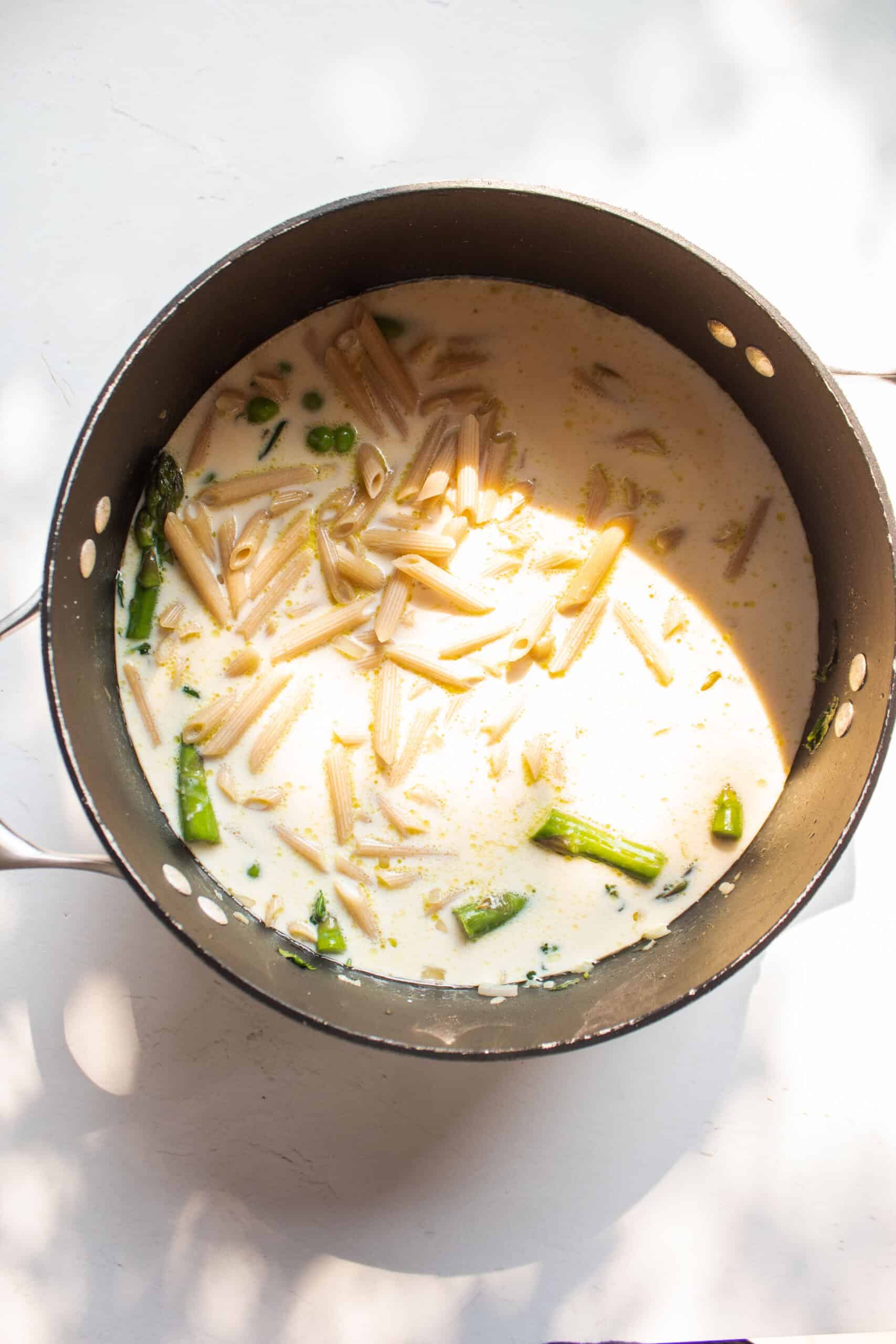 Pasta in a pot with milk, broth, and sauteed veggies.