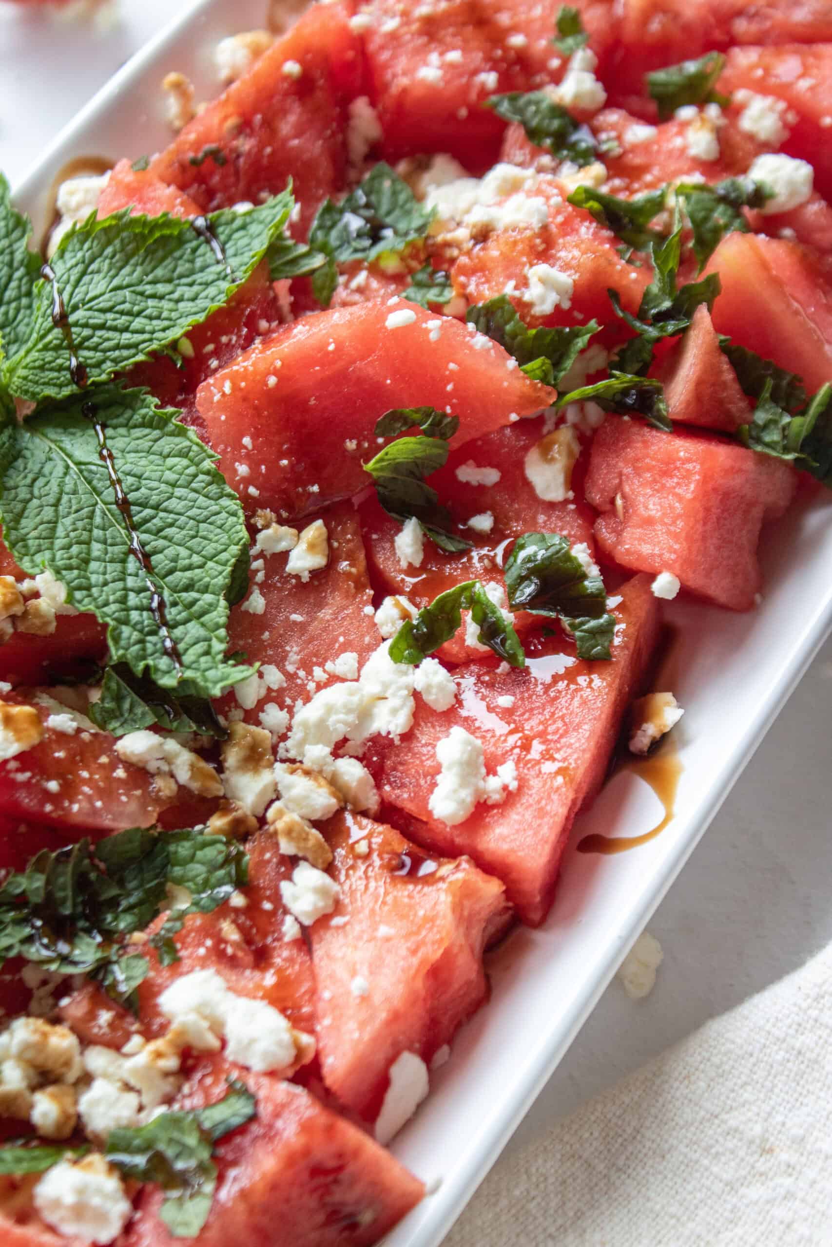 Close up angled shot of a watermelon salad with feta and mint on a plate with balsamic drizzled on top.