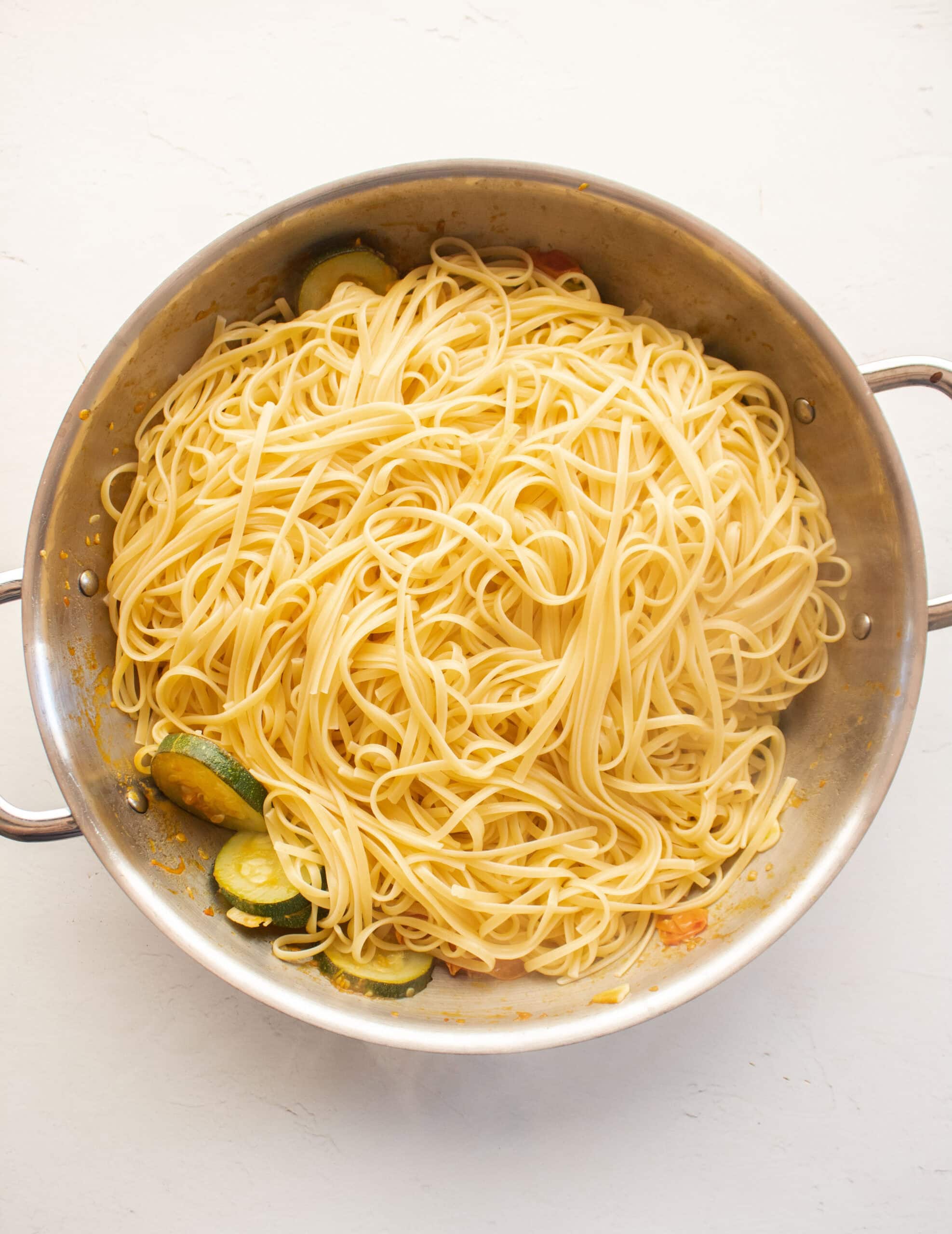 Linguine pasta in a large frying pan with garlic tomatoes and zucchini.