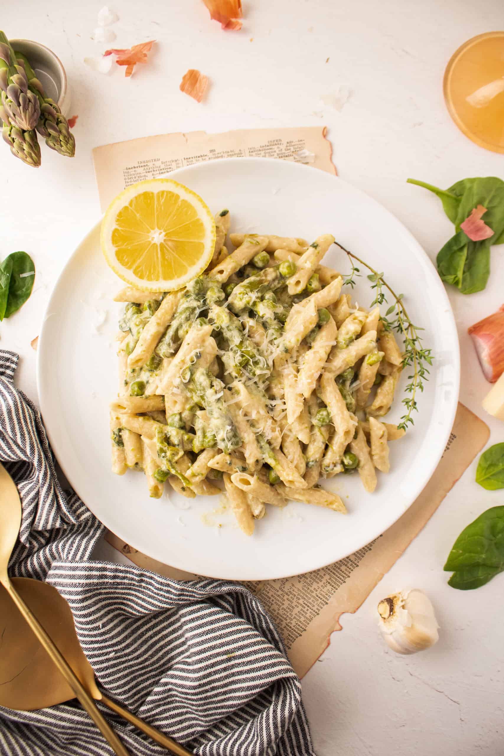 Penne pasta on a plate with asparagus, spinach, and peas.