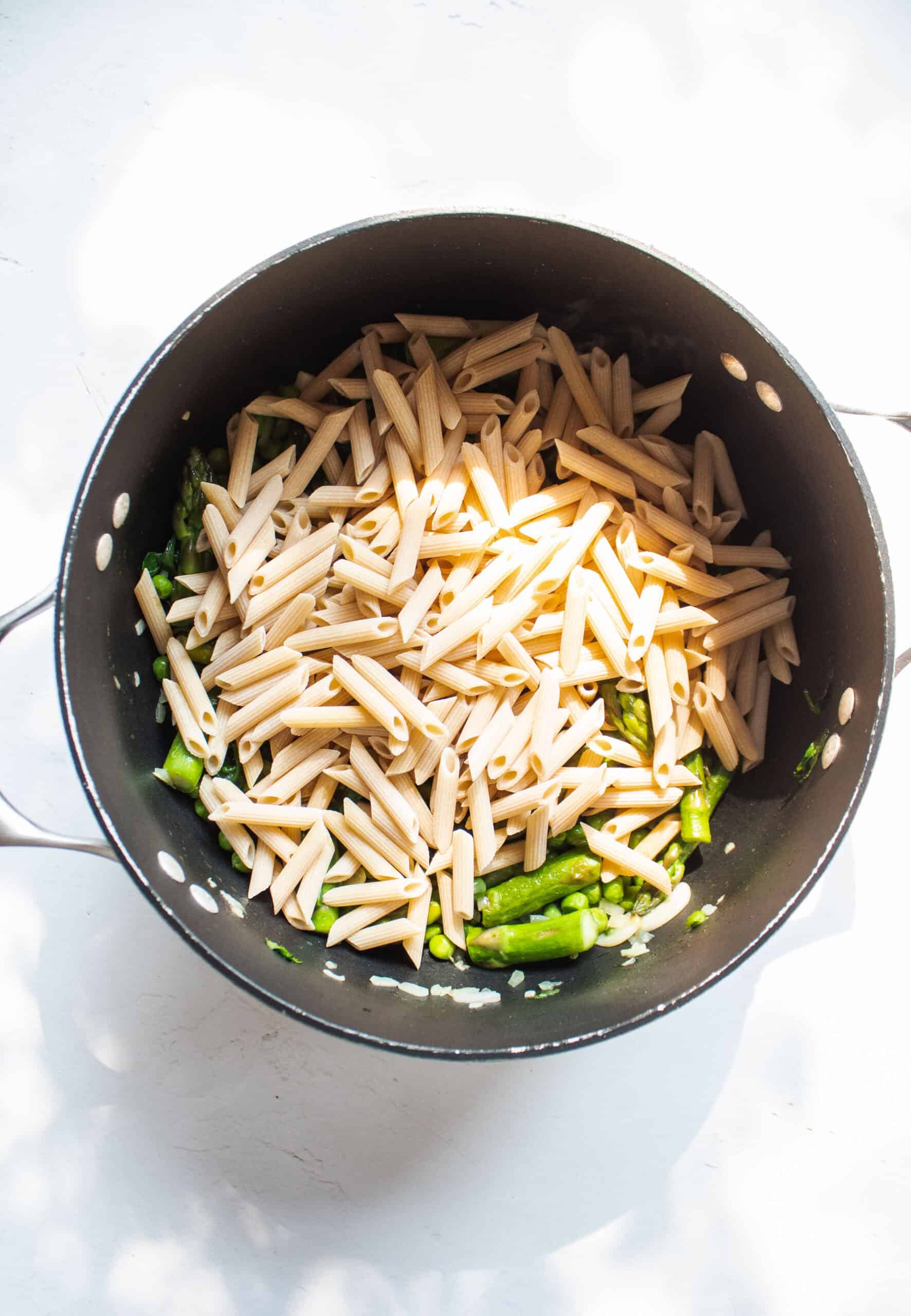 Pasta added to a large pot with sauteed vegetables.