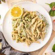 Penne pasta on a plate with asparagus, spinach, and peas.