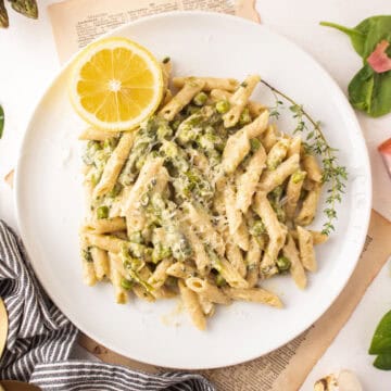 Penne pasta on a plate with asparagus, spinach, and peas.