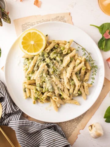 Penne pasta on a plate with asparagus, spinach, and peas.
