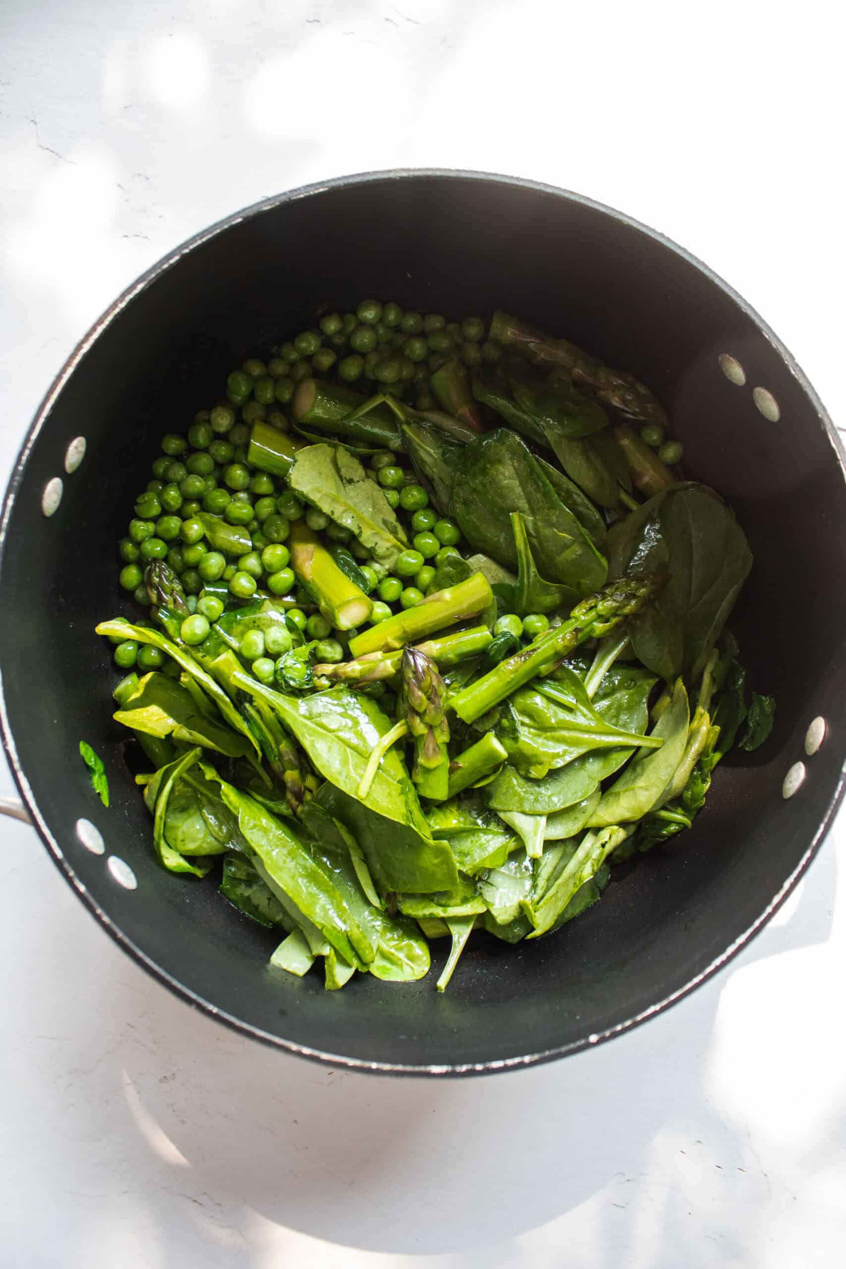 Asparagus, peas, and spinach in a large pot with oil.