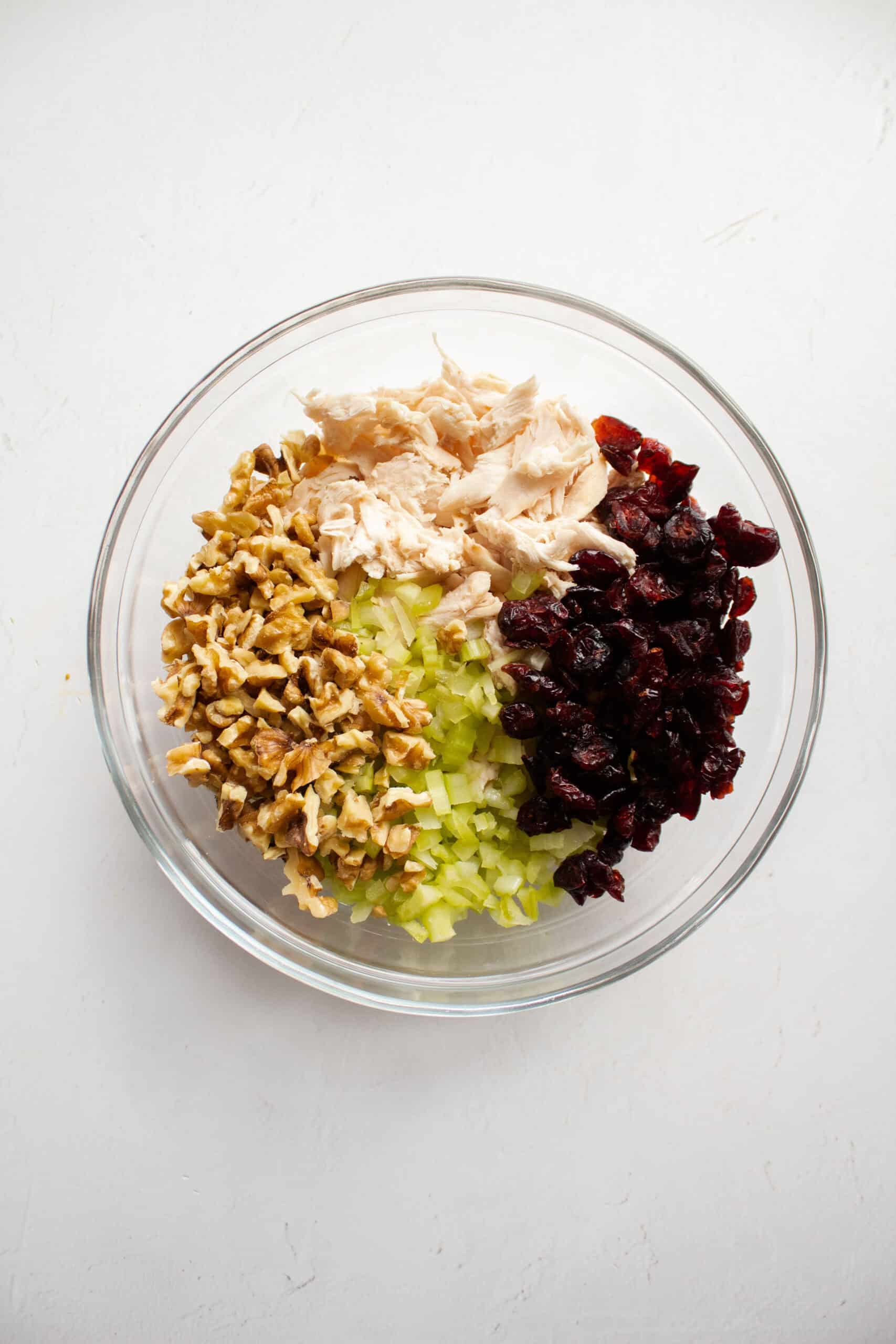 Shredded chicken, walnuts, craisins, and celery in a large mixing bowl.