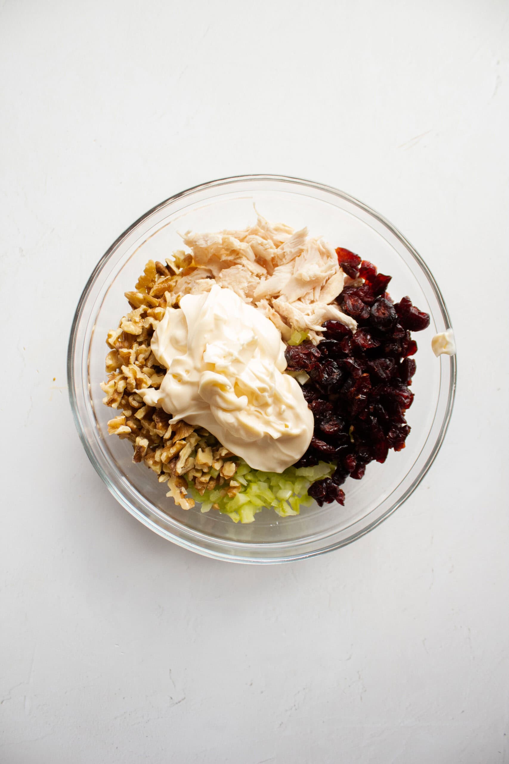 Shredded chicken, walnuts, craisins, and celery in a large mixing bowl topped with mayonnaise.