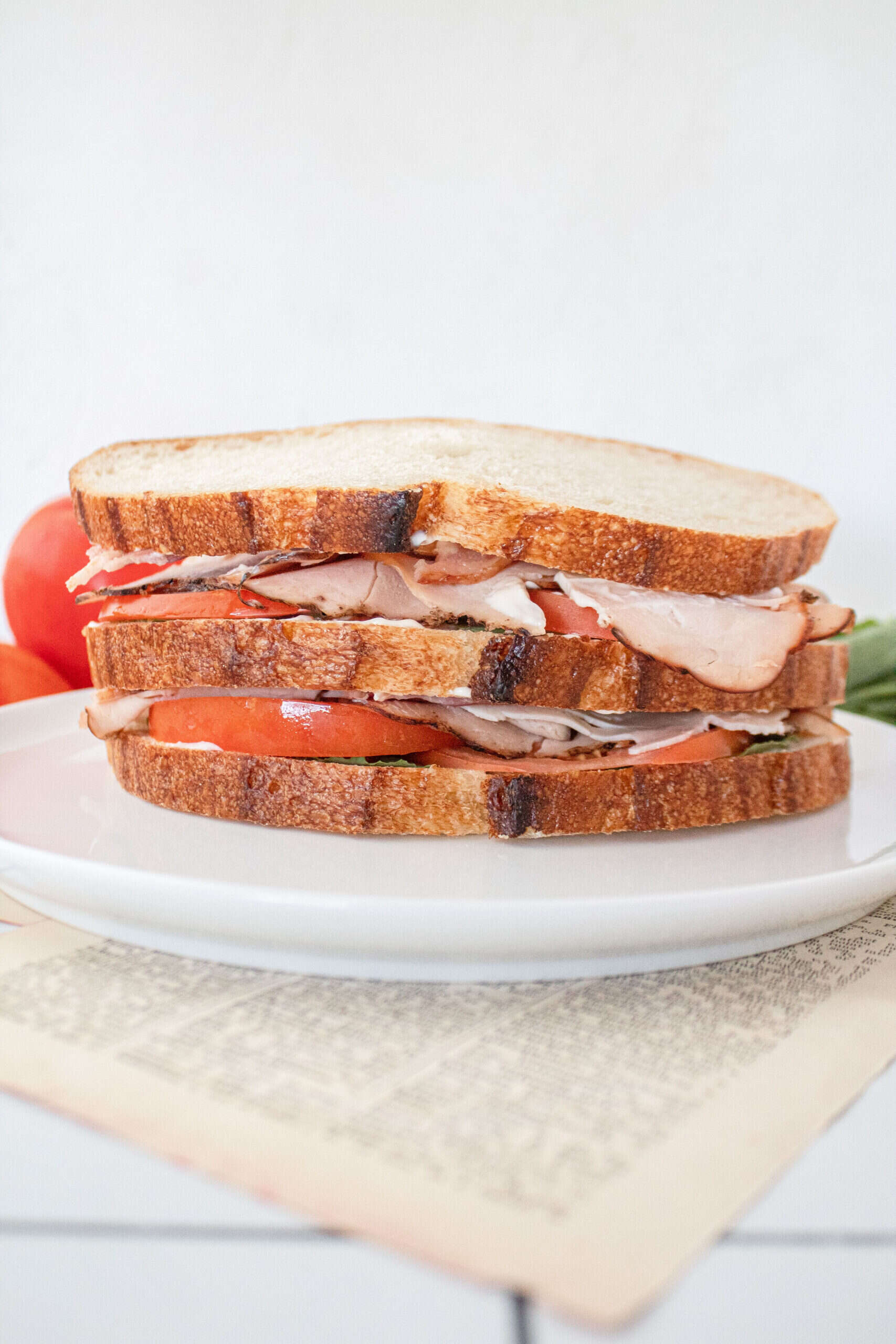 A turkey club sandwich on a plate unsliced.