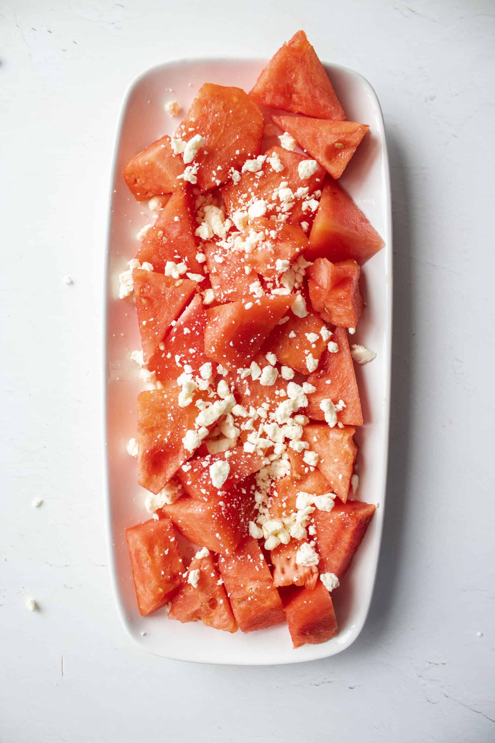 Fresh cut watermelon chunks on a plate with feta.
