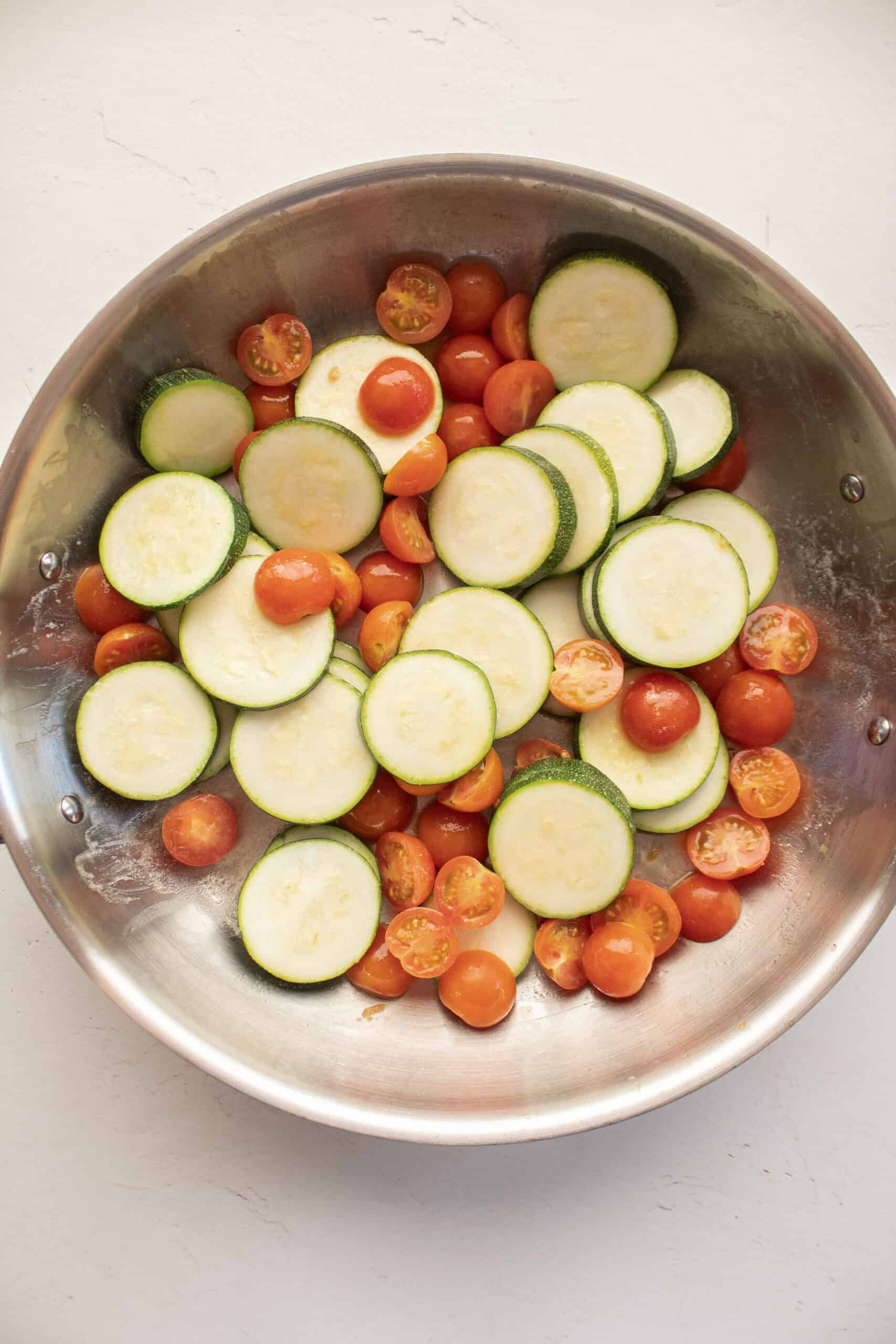 Zucchini and tomatoes in a large frying pan with butter.
