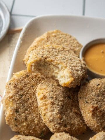a chicken nugget bitten into on top of other chicken nuggets on a plate.