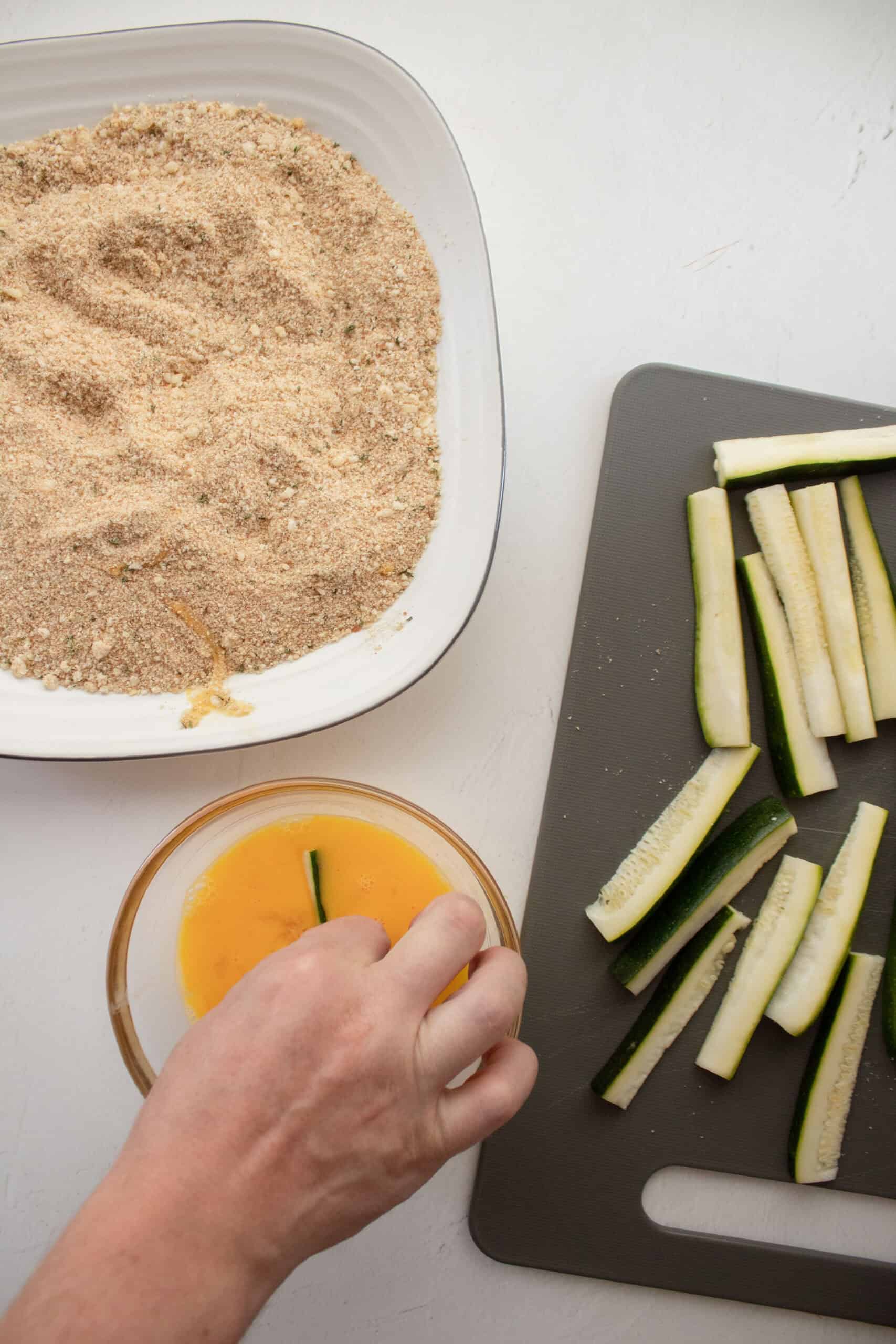 A zucchini fry being dipped in egg.