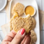 a hand holding a chicken nugget dipped into sauce with a bite missing,