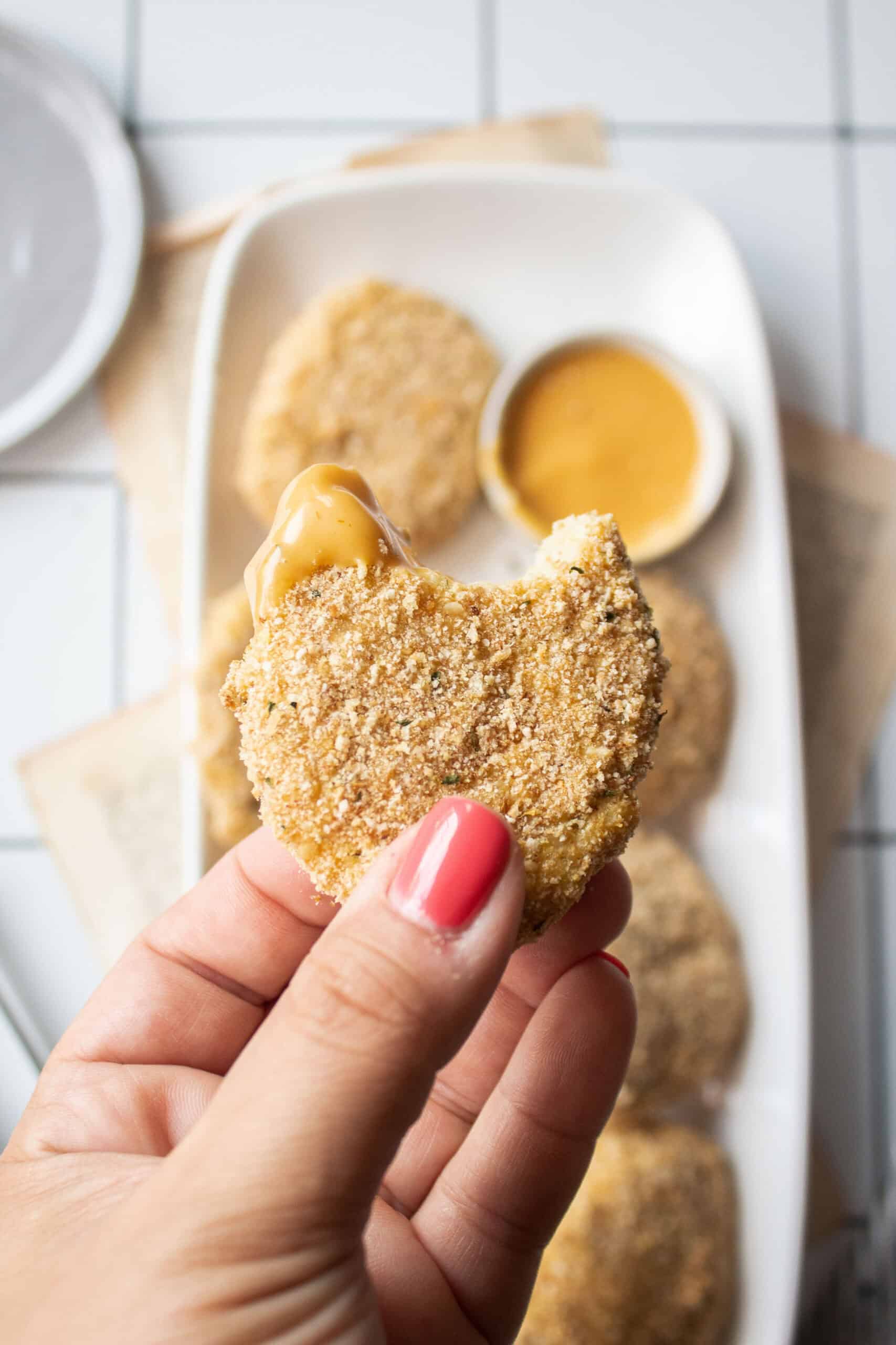 a hand holding a chicken nugget dipped into sauce with a bite missing,