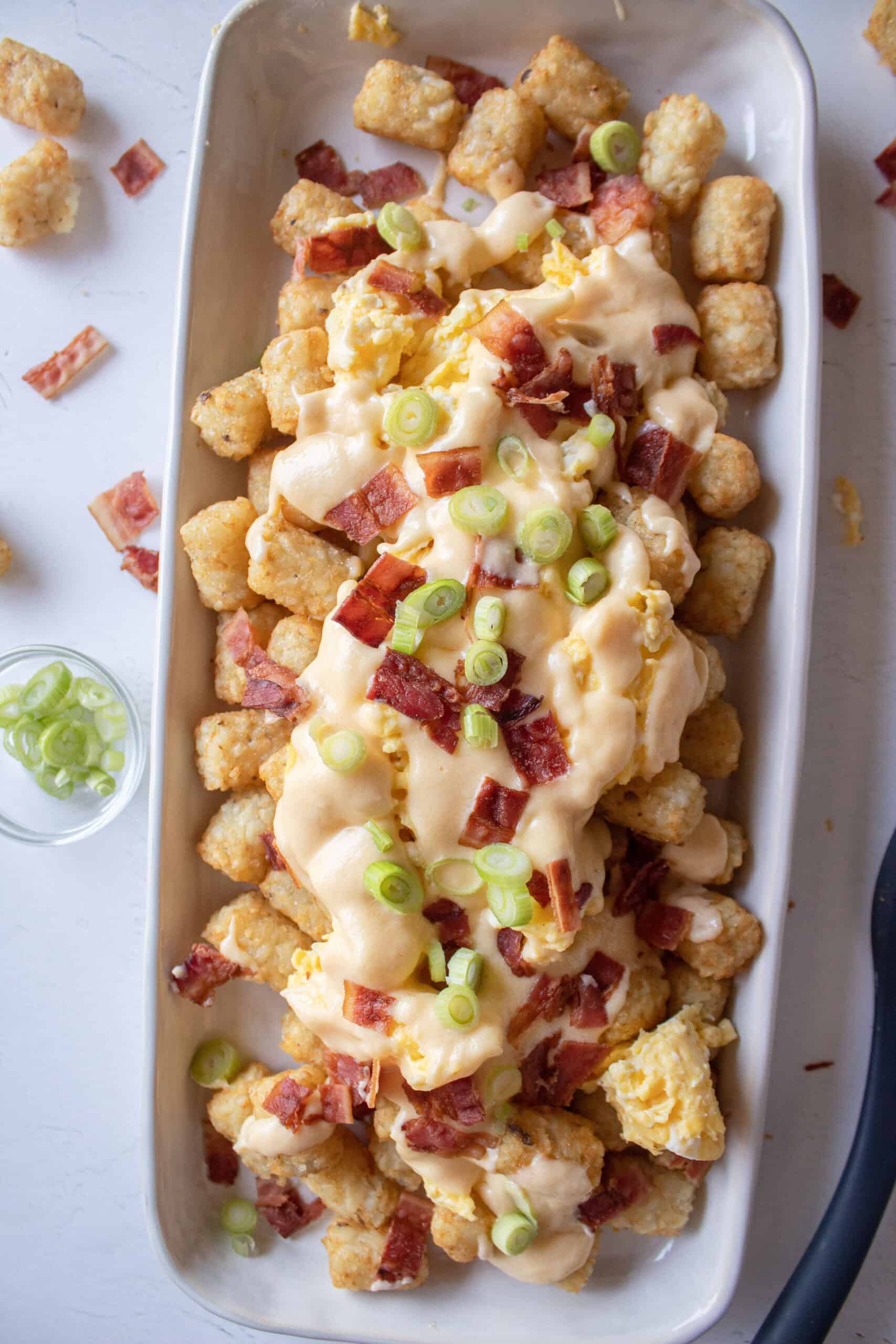 Baked tater tots topped with scrambled eggs, cheese sauce, scallions and bacon.