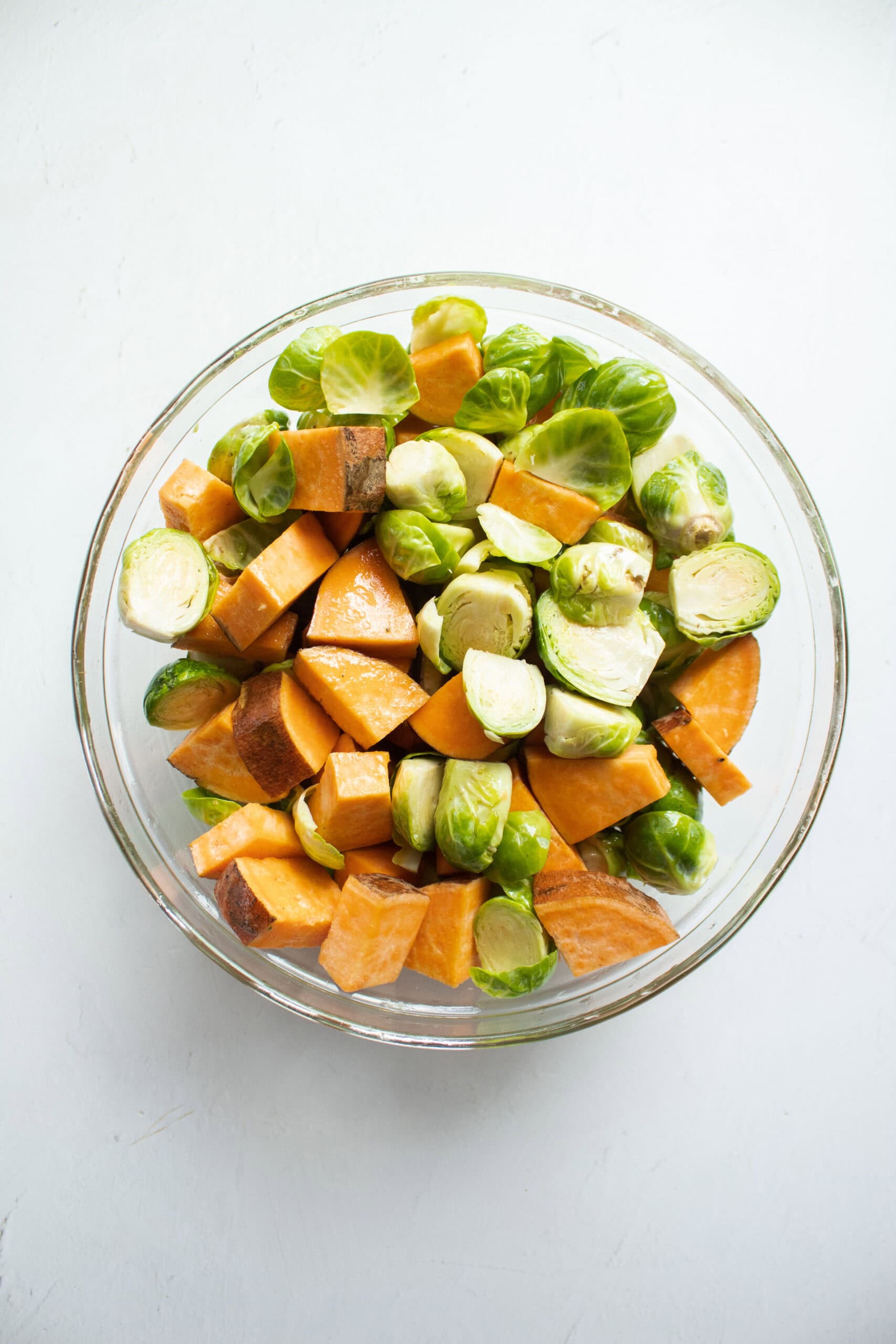 Chopped sweet potatoes and halved brussels sprouts in a large mixing bowl with olive oil, salt, and pepper.